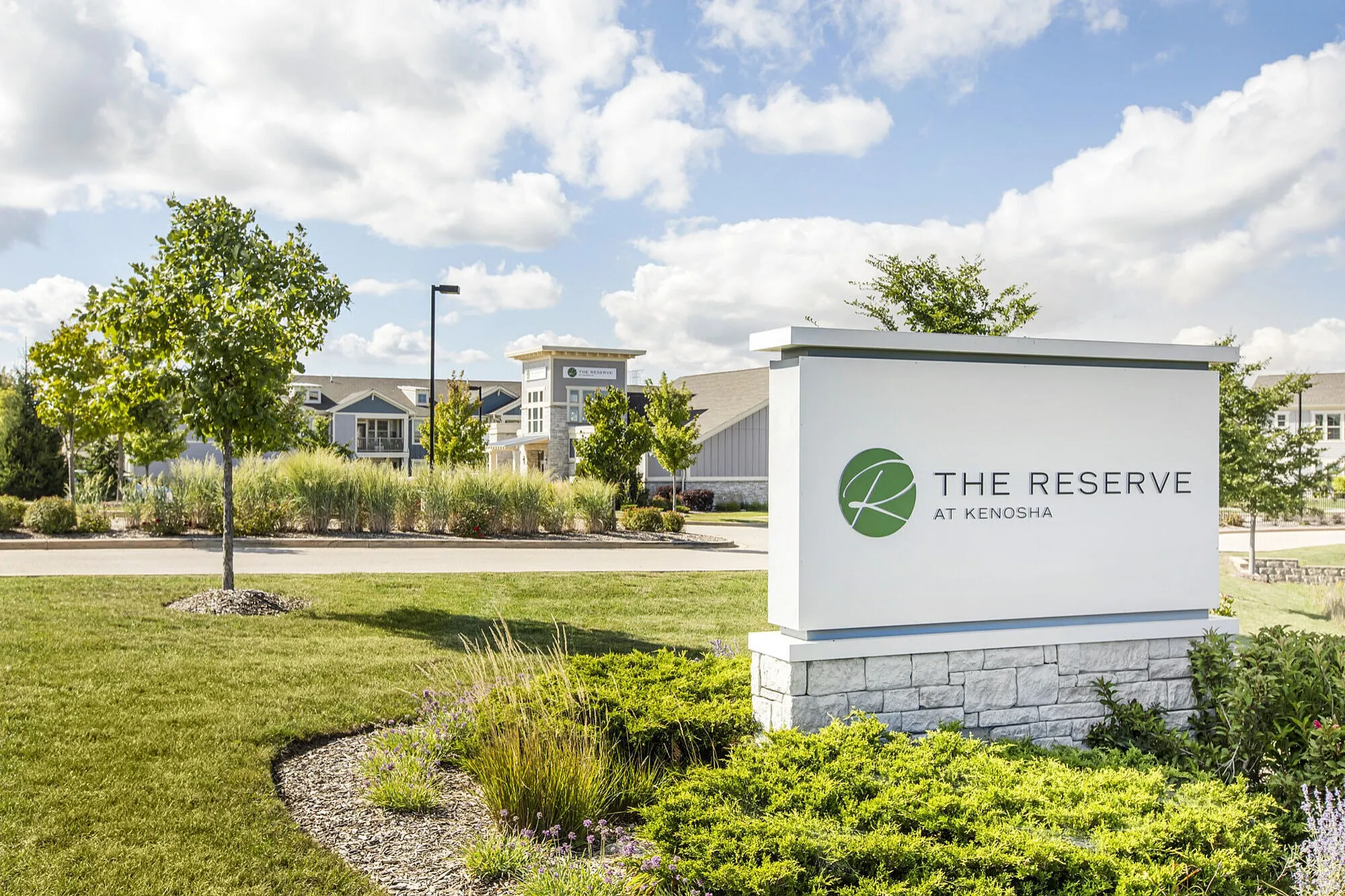 Charming exterior view of The Reserve at Kenosha, featuring lush landscaping and elegant architecture under a bright blue sky.