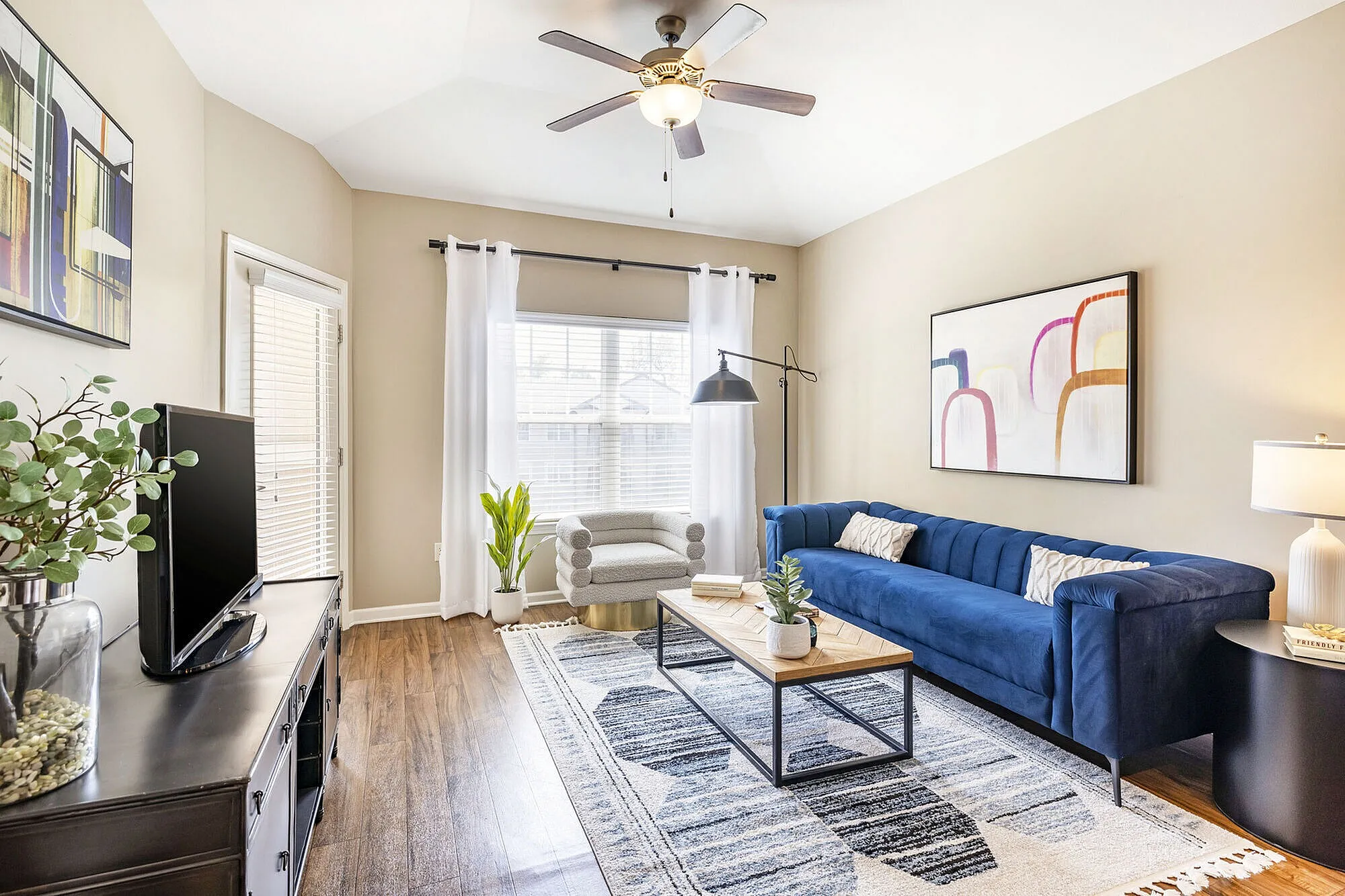 Inviting living room with elegant blue sofa, modern decor, and natural light pouring through large windows.