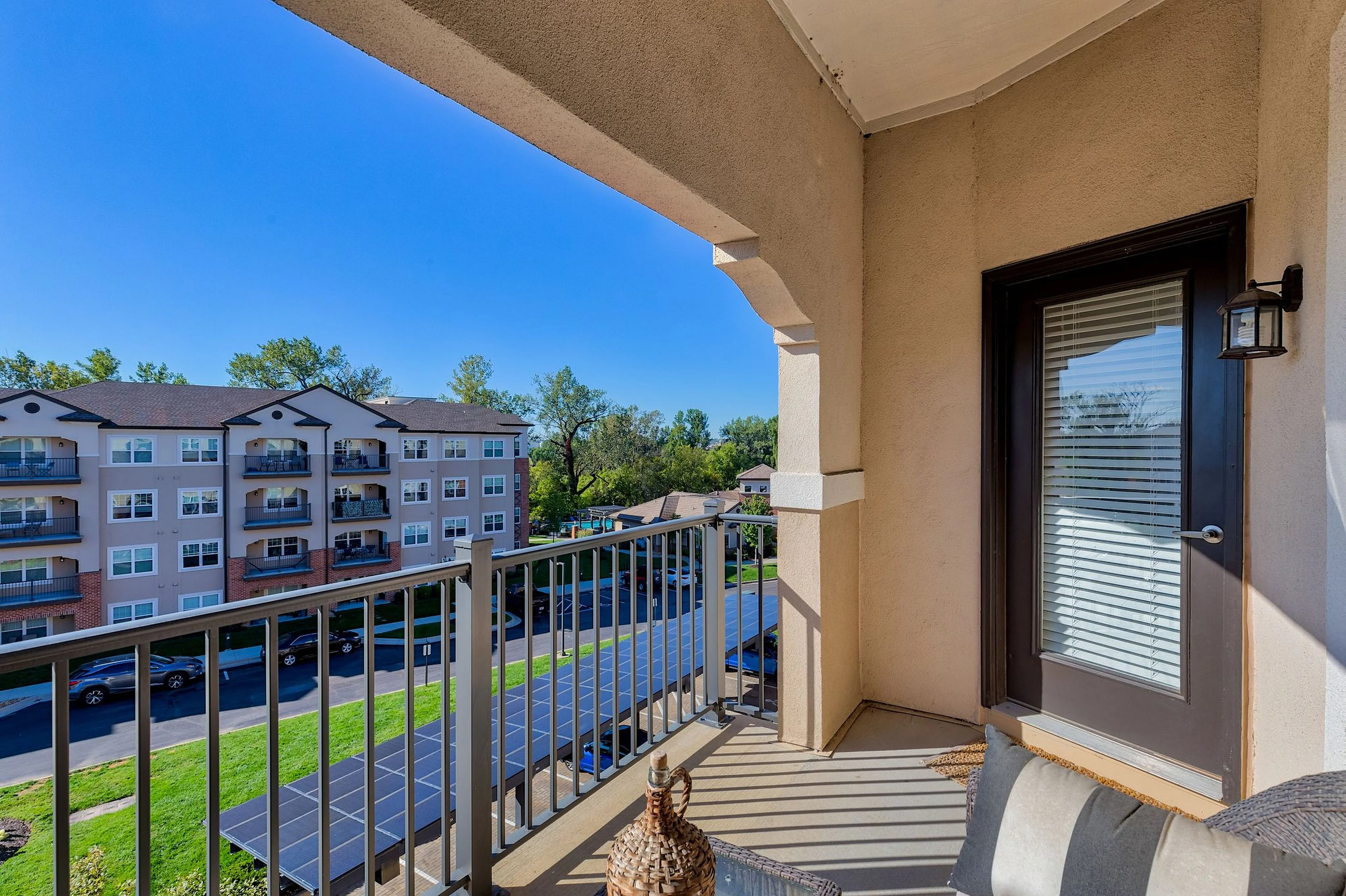 Charming apartment balcony with scenic view of modern apartment complex, lush greenery, and bright blue skies.