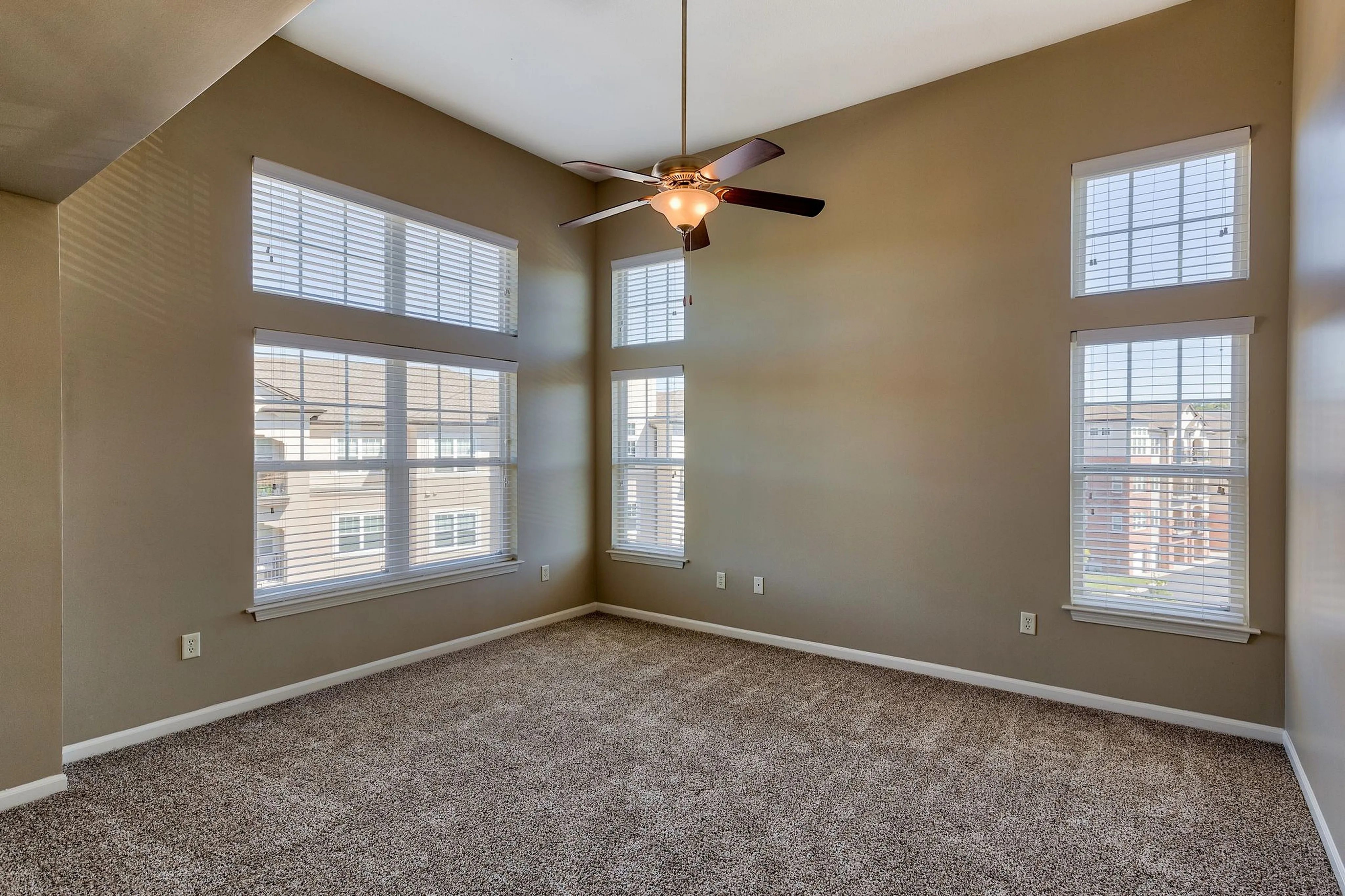 Bright and airy empty room with plush carpeting, large windows, and a stylish ceiling fan, perfect for customization.