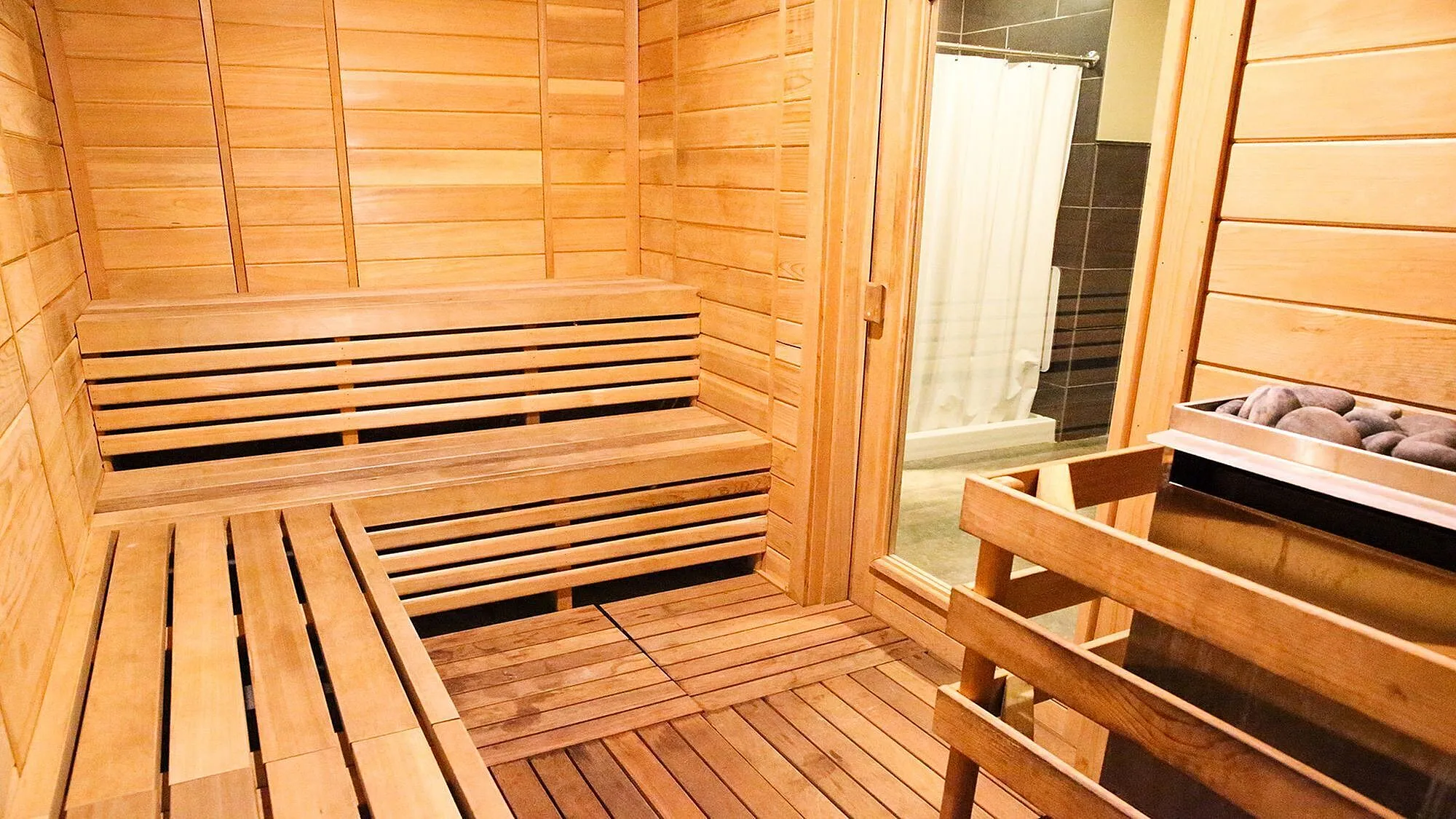 Luxurious wooden sauna room with bench seating and a stone heater, perfect for relaxation and wellness.