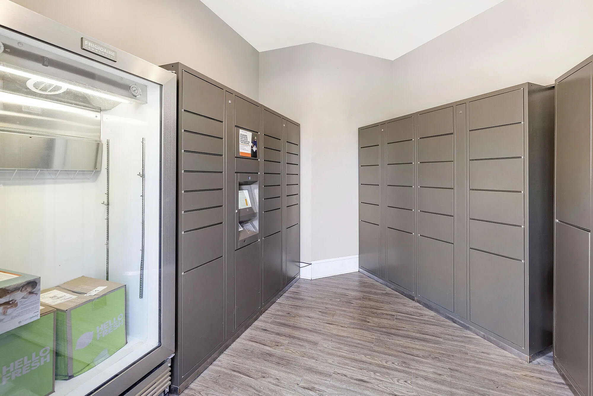 Modern package delivery room featuring sleek storage lockers and a glass-front fridge in a secure apartment complex.
