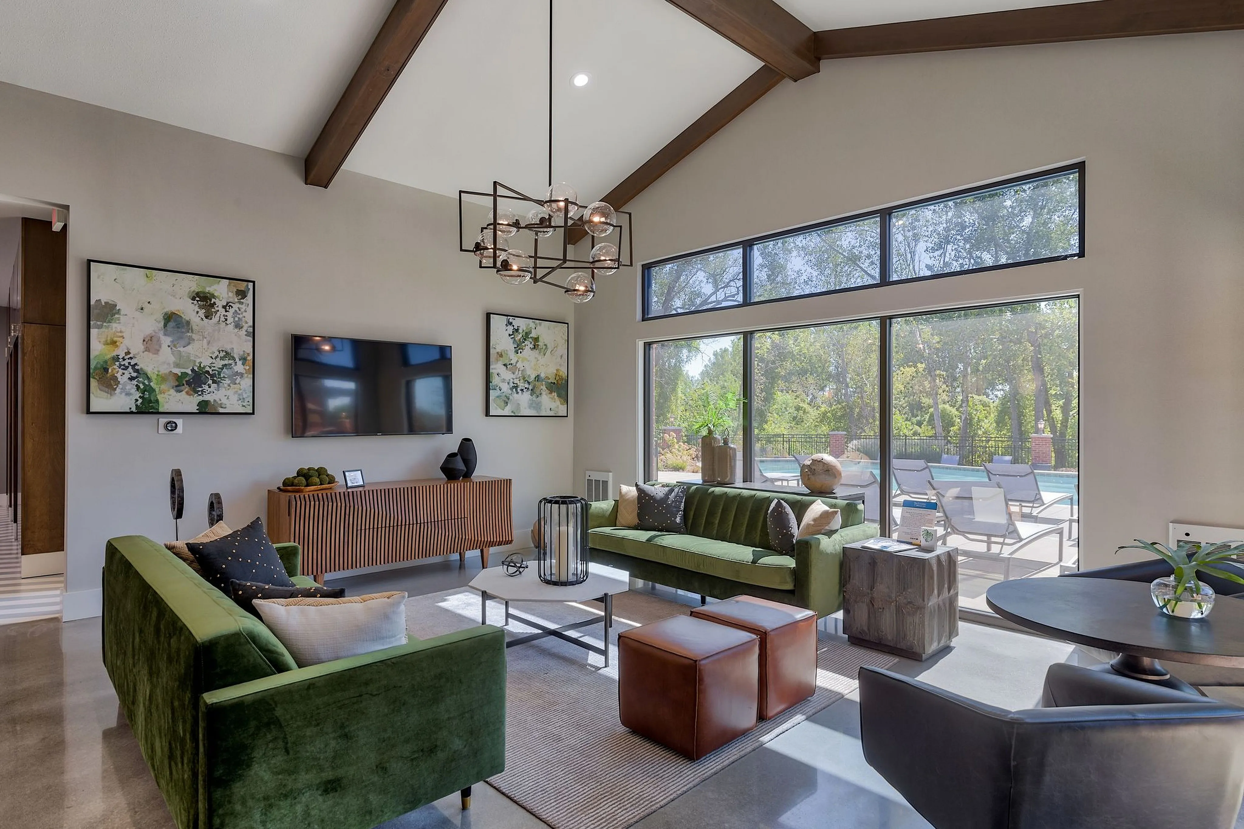 Chic living room with high ceilings, modern chandelier, and large windows overlooking a lush garden and pool.