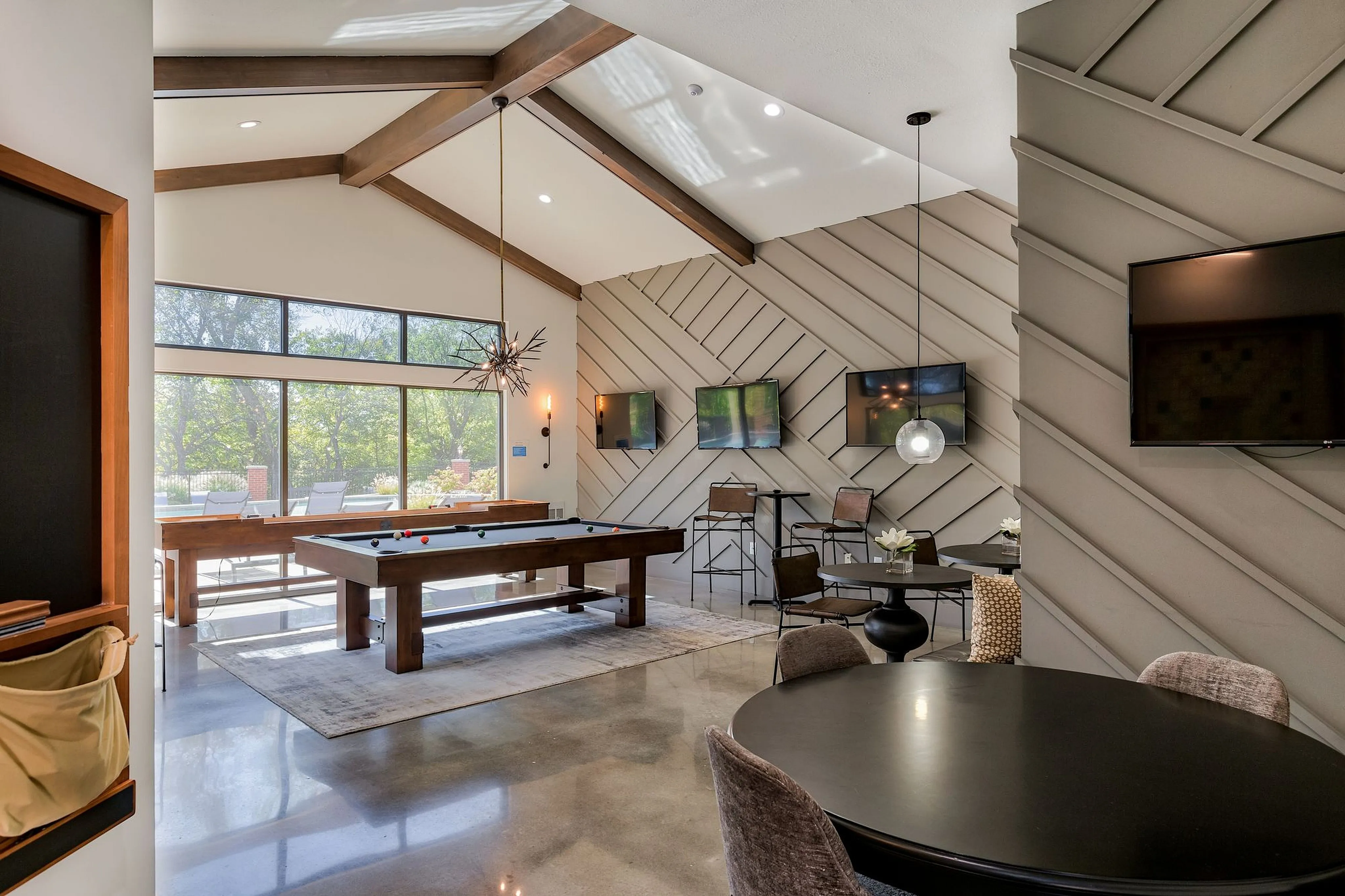 Elegant open-concept recreational area featuring a stylish pool table, modern decor, and large windows with serene garden views.
