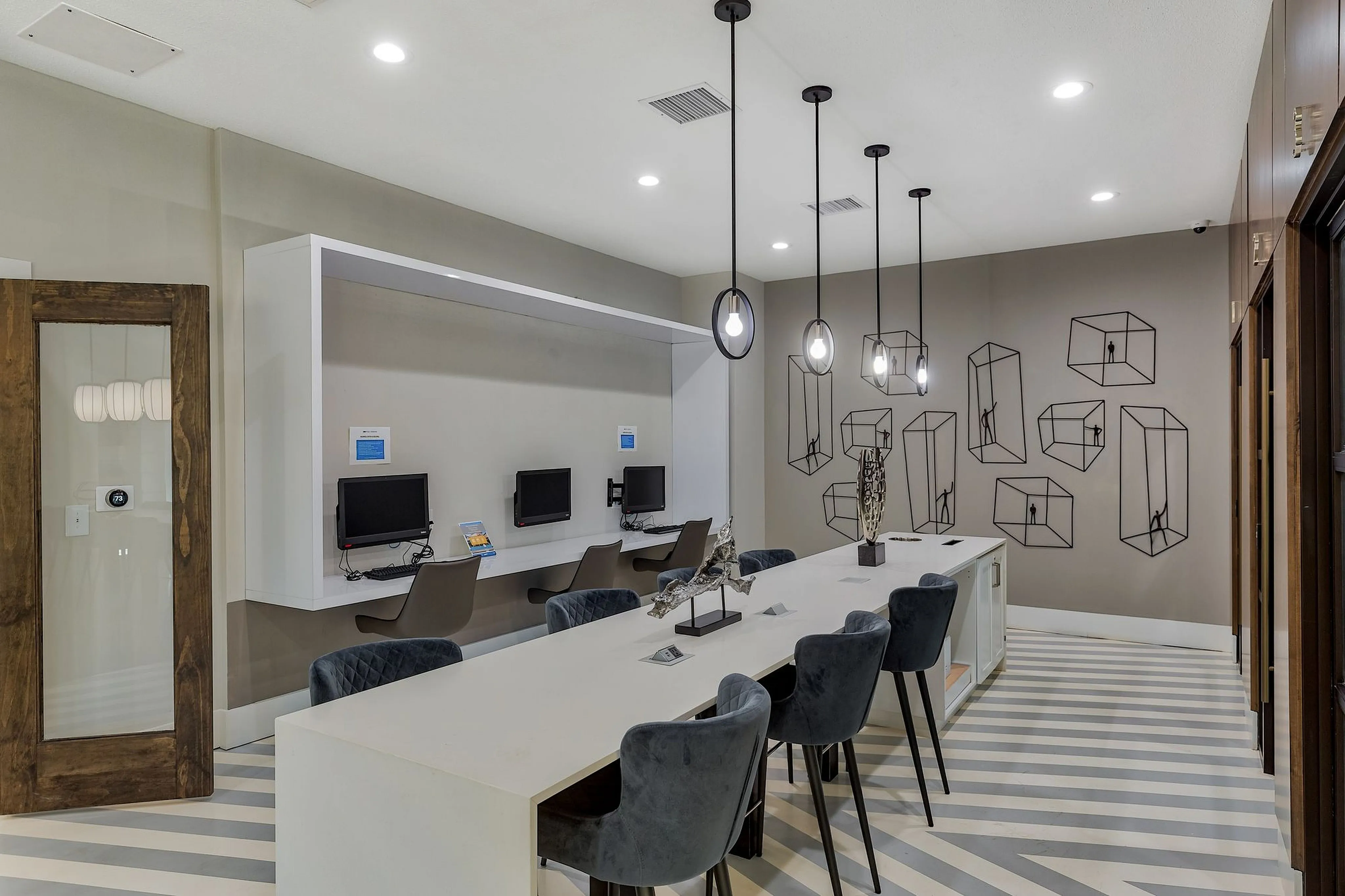 Modern communal workspace with sleek computers, geometric wall art, and chic hanging lights, perfect for productivity.
