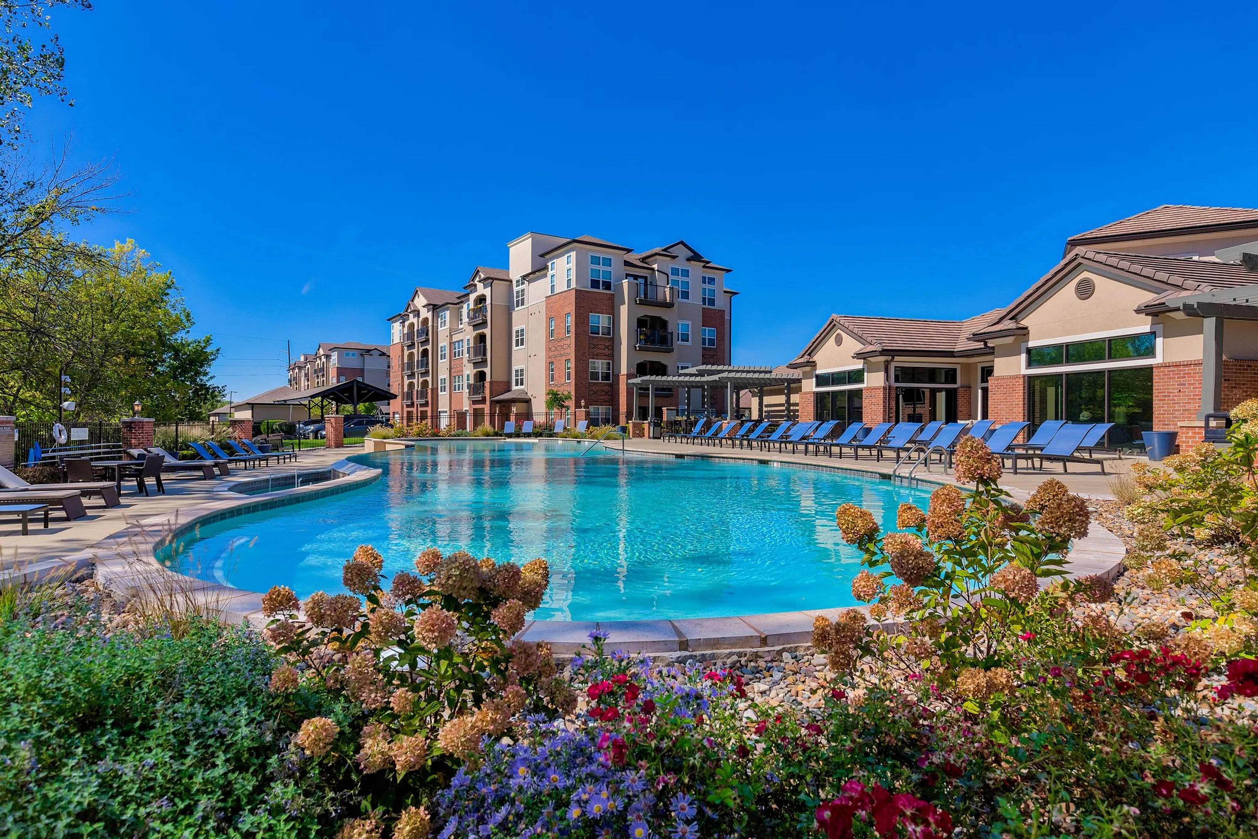 Luxurious apartment complex with a stunning outdoor pool surrounded by lush gardens and modern amenities.