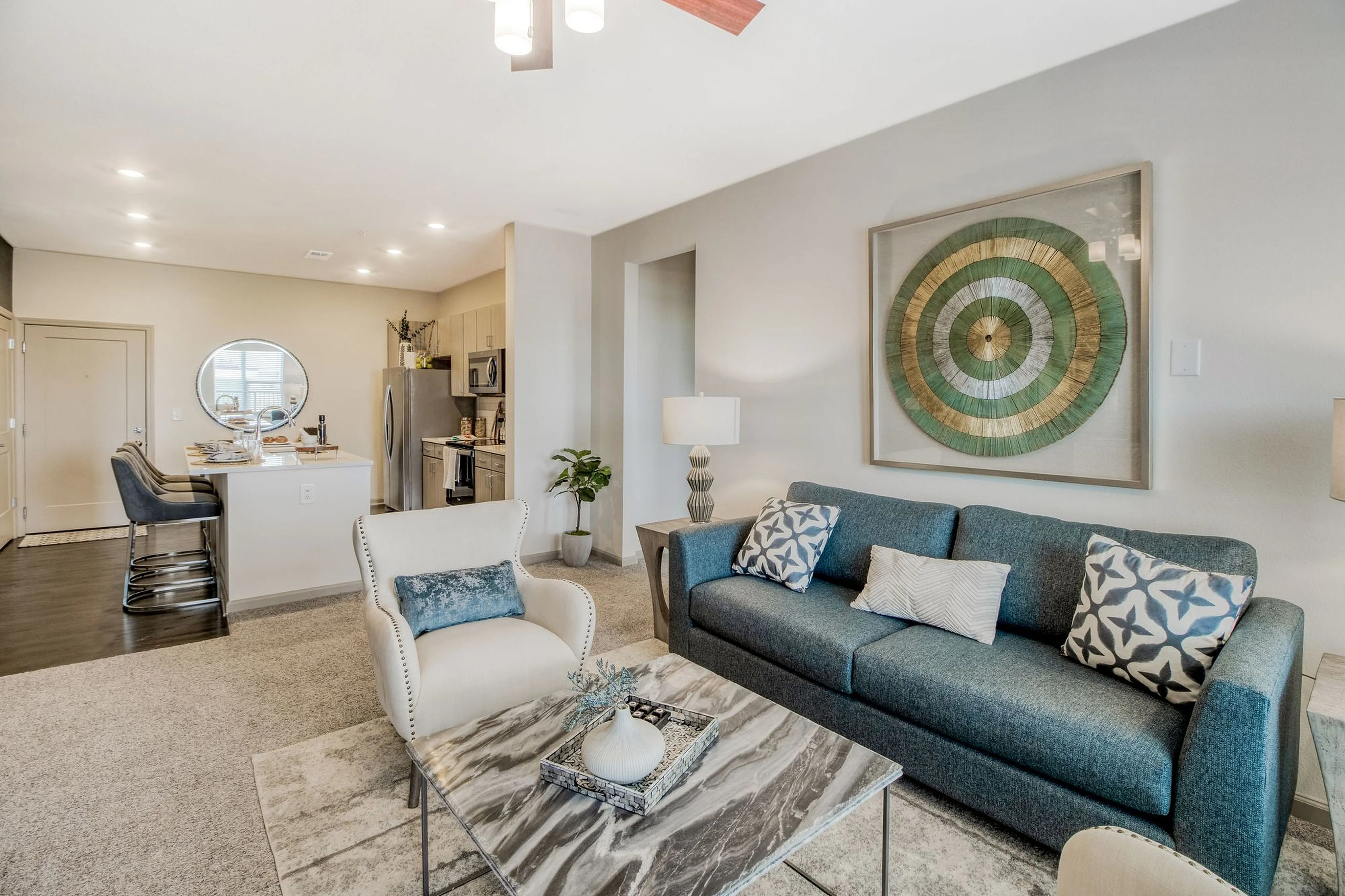 Bright and modern open-concept living space with elegant decor, featuring a cozy blue sofa, stylish armchair, and sleek kitchen with stainless steel appliances.