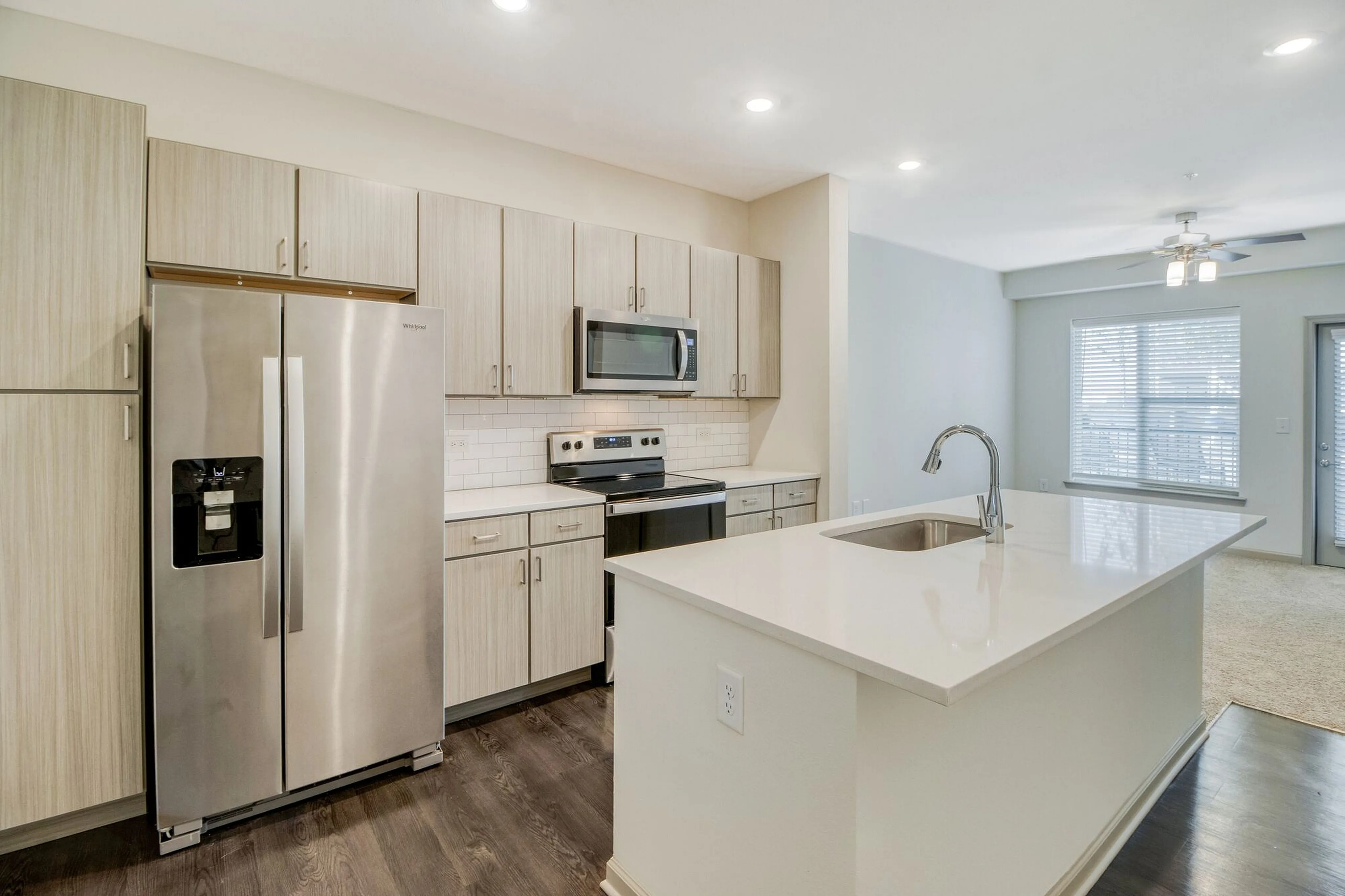 Modern kitchen with sleek stainless steel appliances, stylish wood cabinetry, and a spacious island overlooking a bright, open living area with large windows.