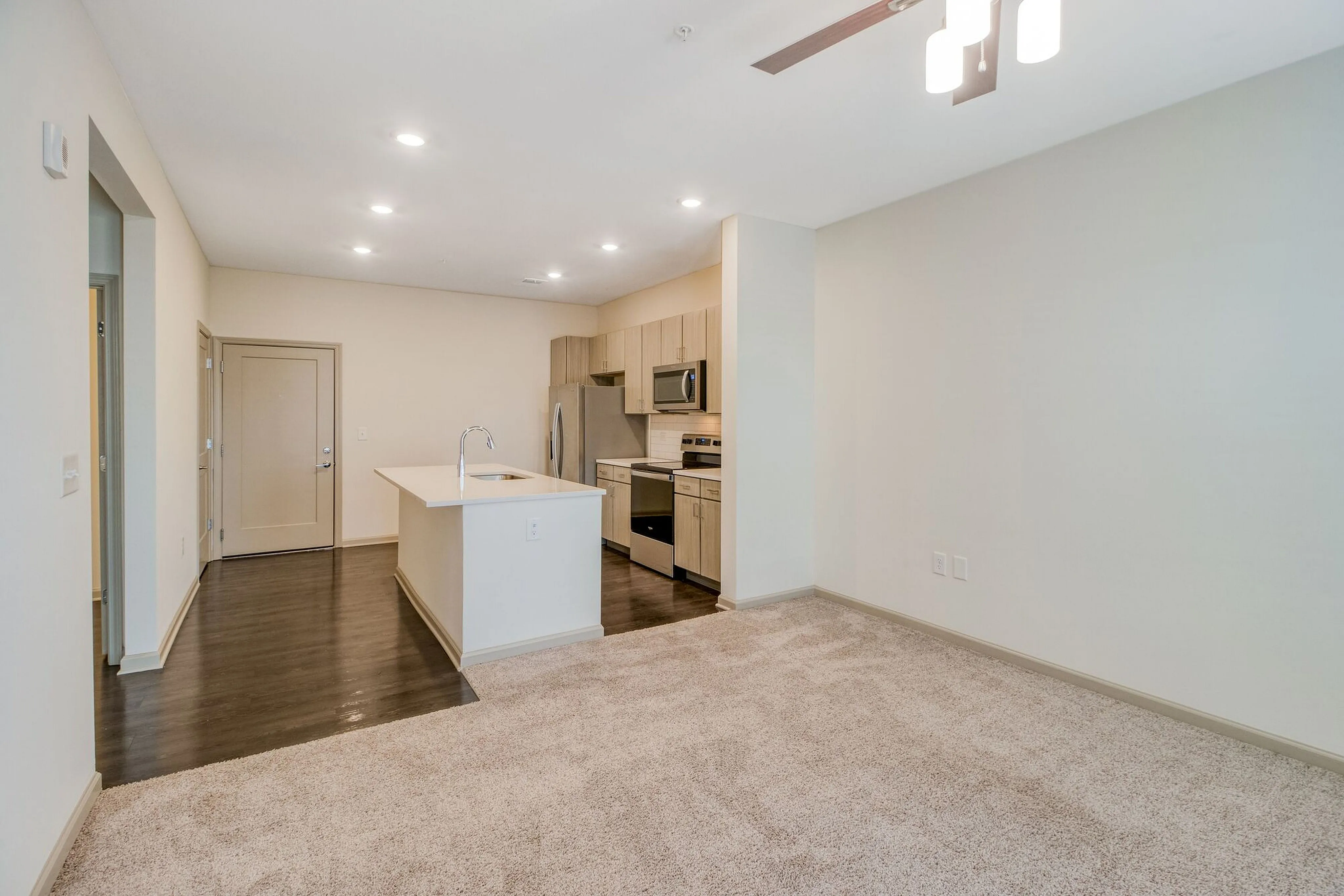 Modern apartment interior featuring an open-concept layout with a sleek kitchen, cozy carpeted living area, and elegant lighting.