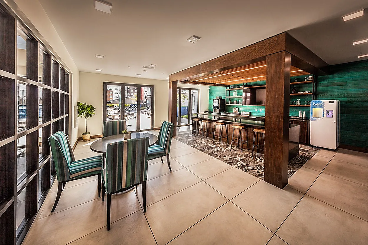 Elegant communal space with stylish seating, modern bar area, and floor-to-ceiling windows opening to an inviting patio.