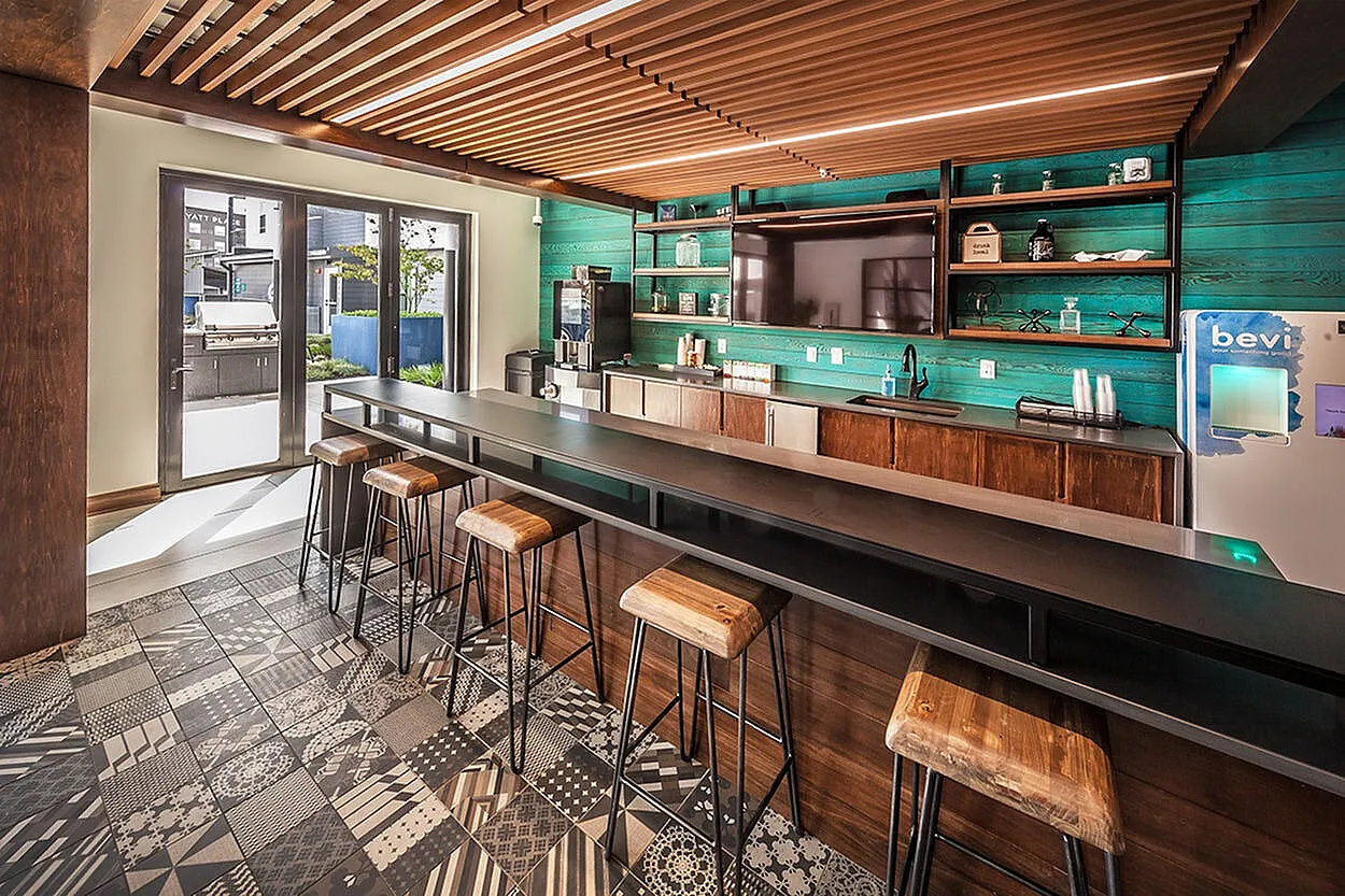 Modern communal kitchen featuring a sleek bar counter, stylish wooden stools, and vibrant teal accent wall, ideal for social gatherings.