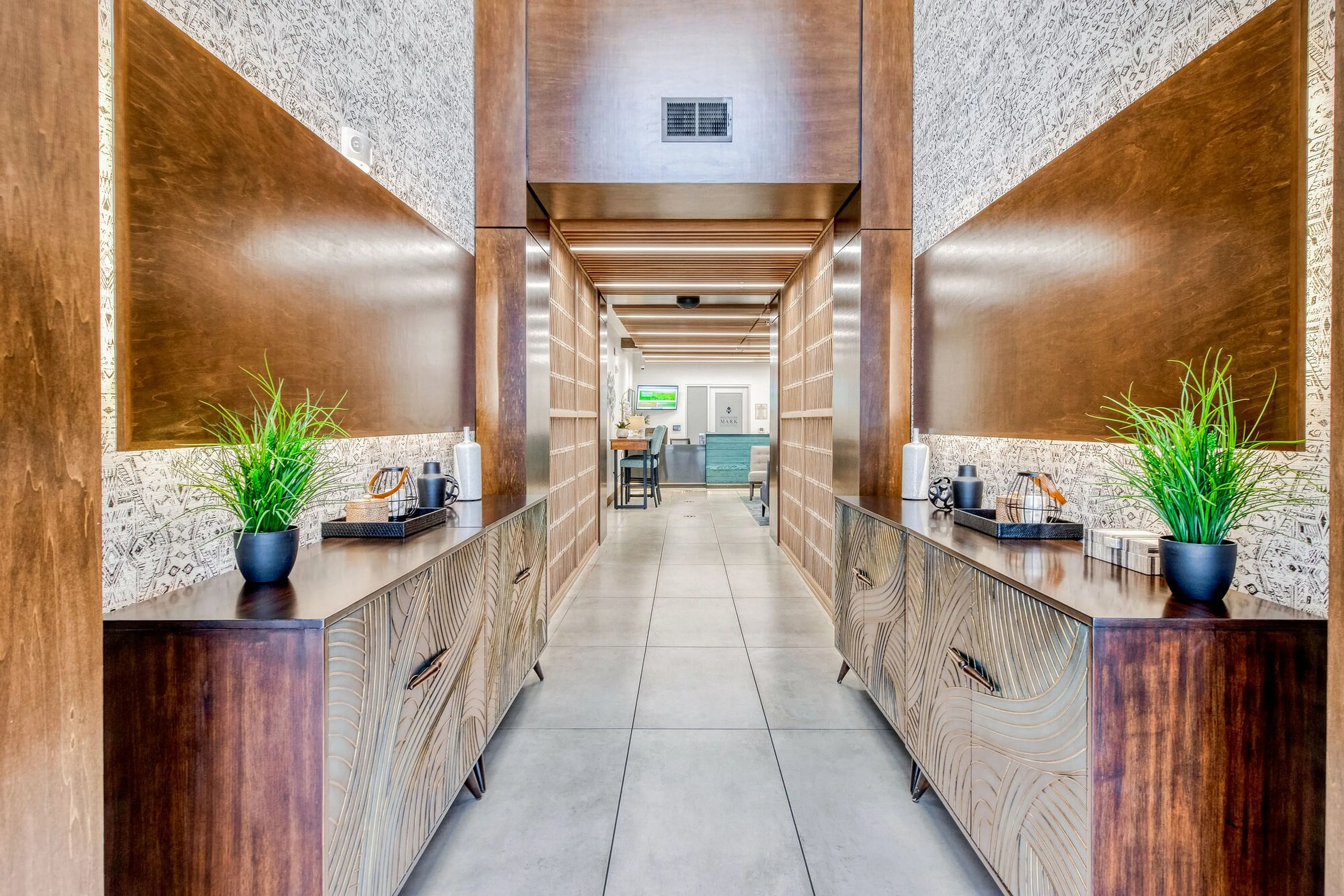 Elegant hallway with modern wood paneling, decorative plants, and sleek cabinetry leading to a welcoming reception area.