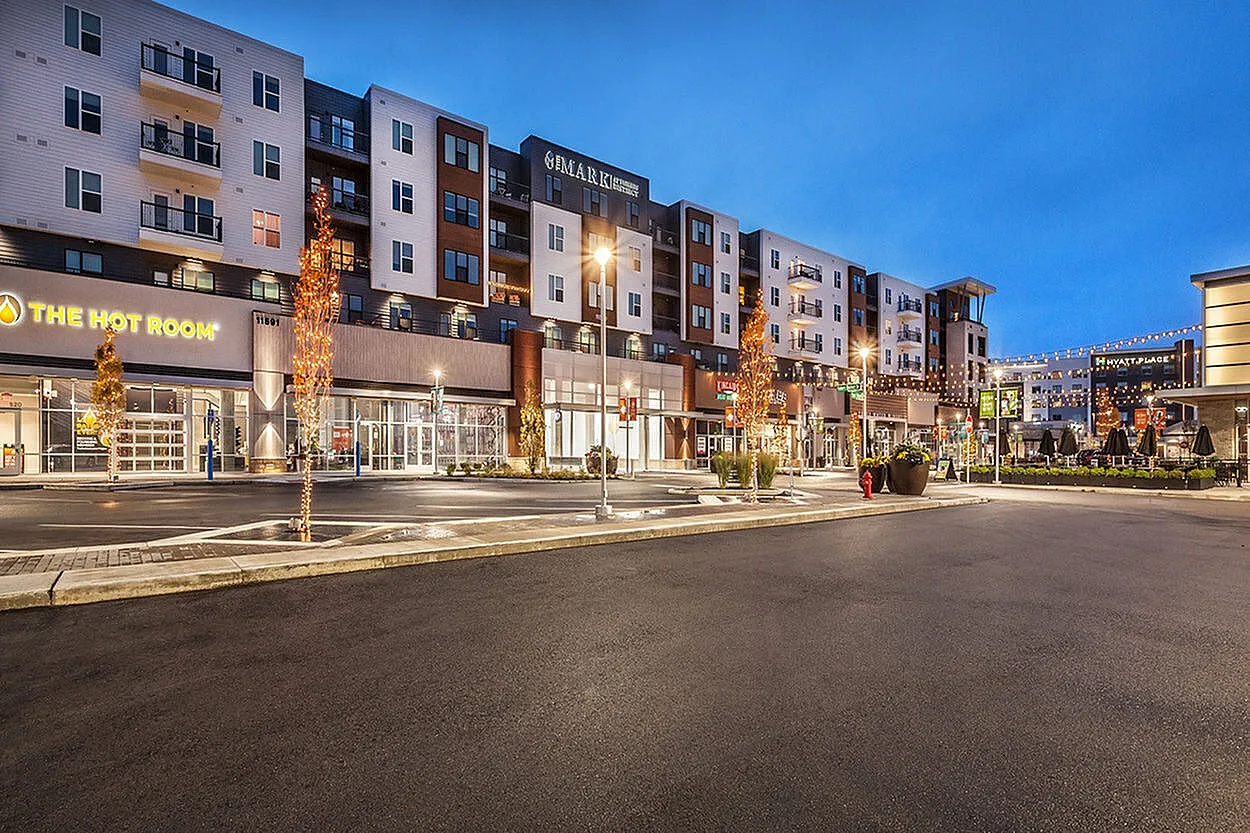 Vibrant modern apartment complex with retail spaces, featuring elegant lighting and appealing architecture in a lively urban setting.