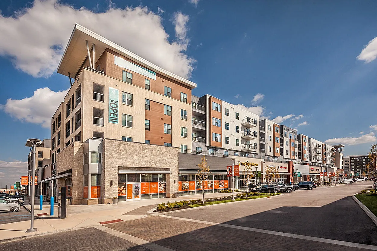 Modern multi-story apartment complex with contemporary design, featuring retail shops on the ground level and balconies overlooking a bustling urban setting.