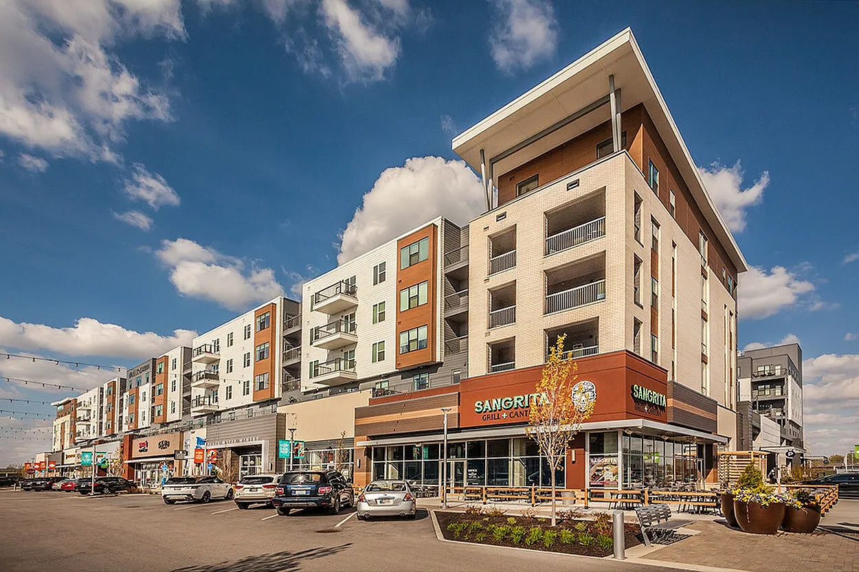 Contemporary apartment building with retail shops on ground level, featuring modern architecture and sunny outdoor spaces.