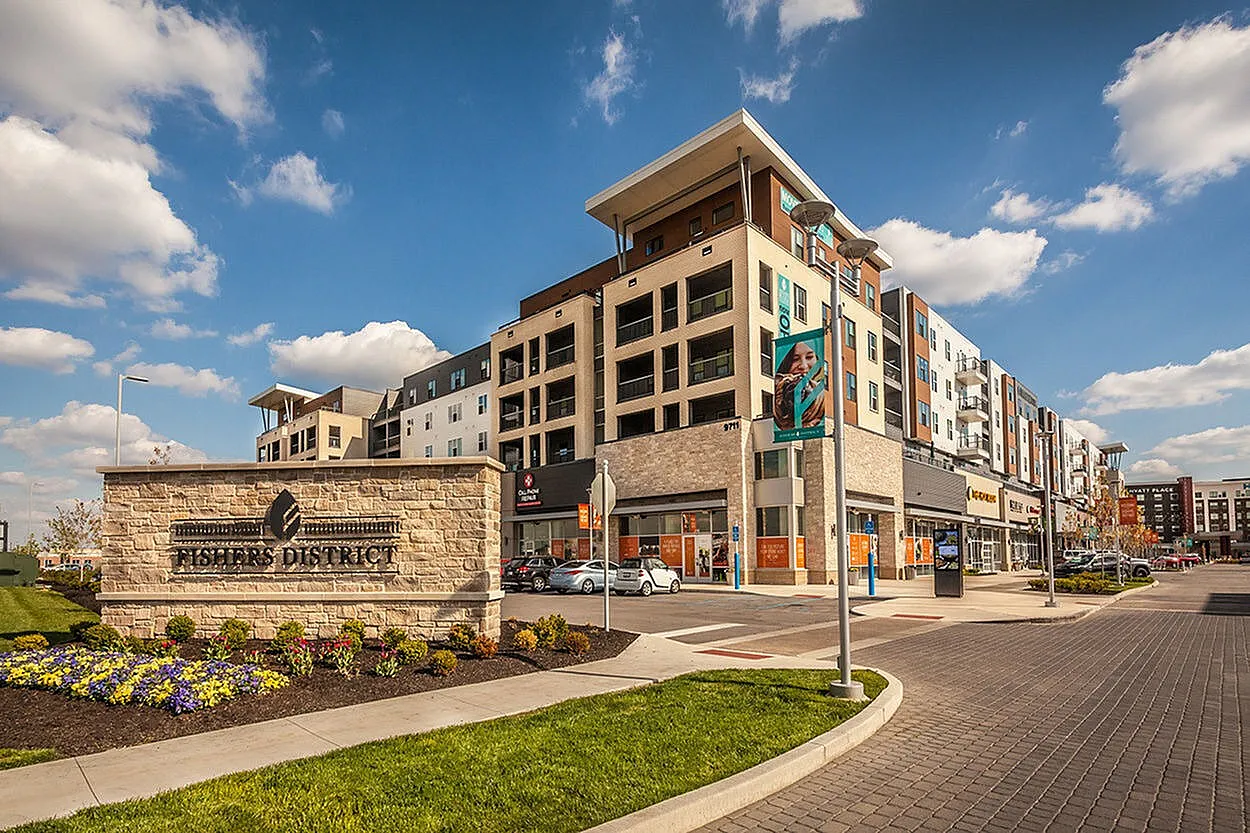 Charming modern apartment complex in Fishers District with vibrant shopping and dining options, bathed in warm sunlight under a clear blue sky.