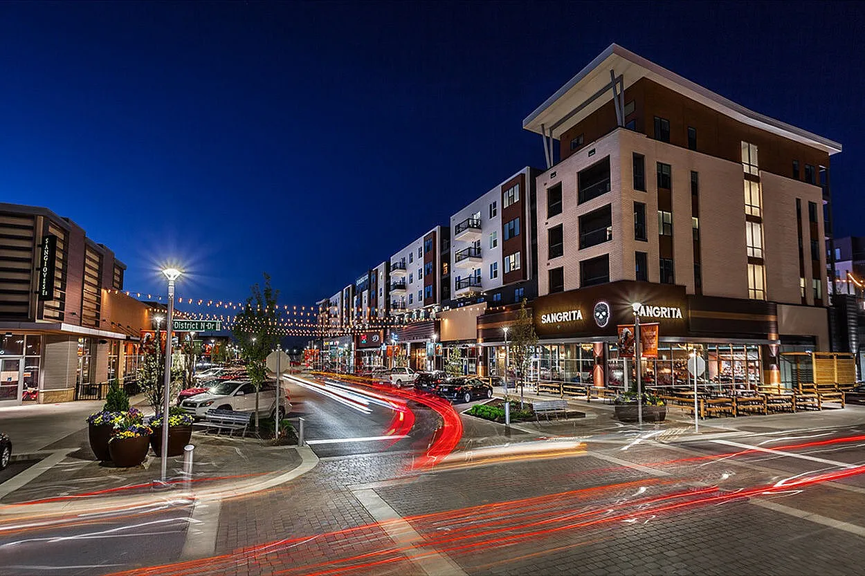 Vibrant nighttime cityscape featuring modern apartment buildings, bustling street, and lively restaurant fronts under sparkling string lights.