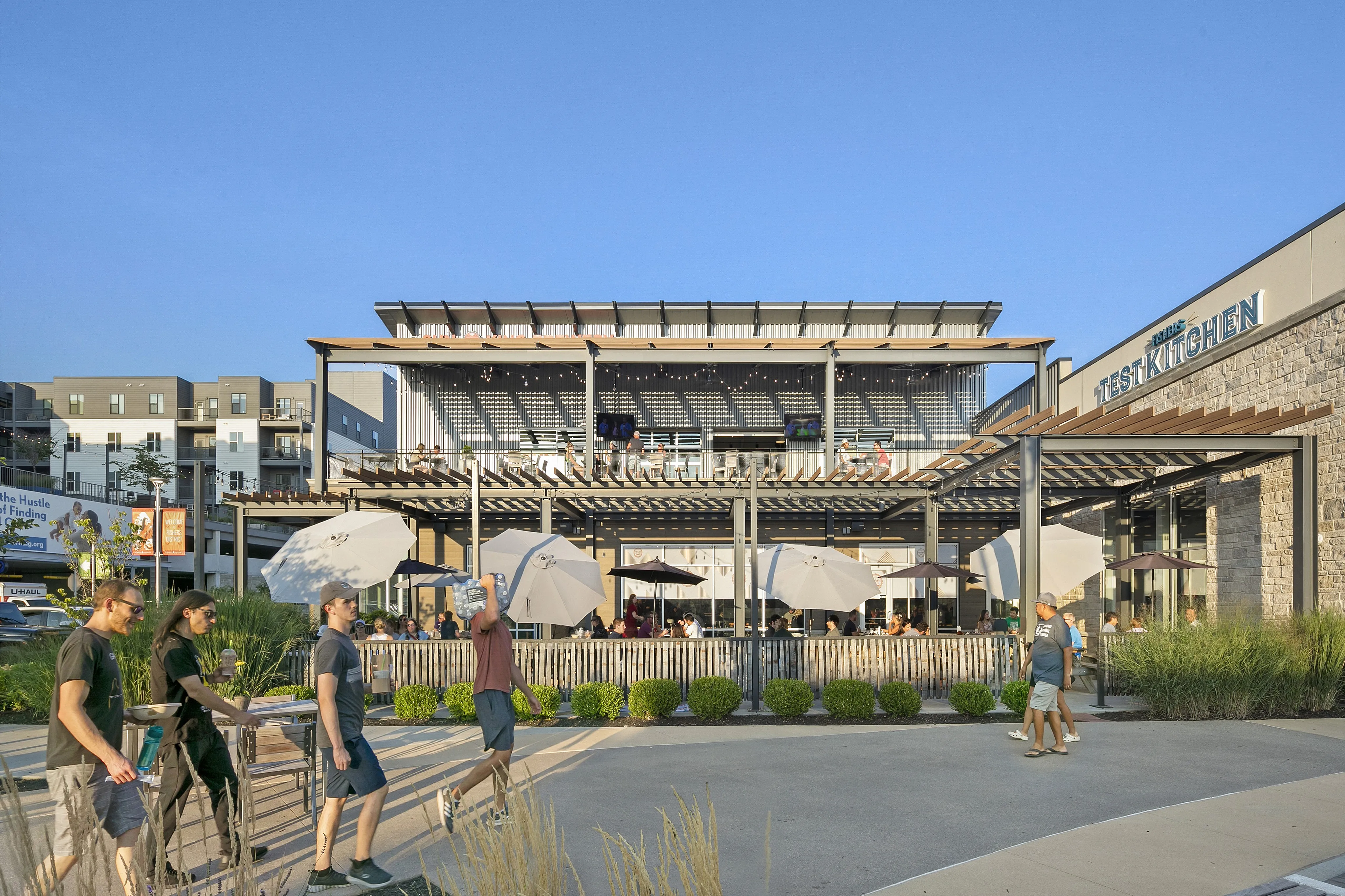 Vibrant outdoor dining area at a modern test kitchen, featuring elegant seating under large umbrellas with a backdrop of contemporary architecture.