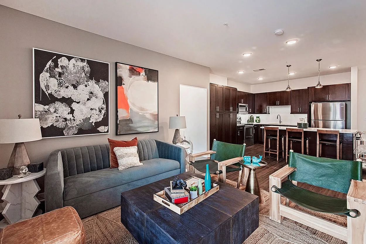 Modern open-plan living room and kitchen with elegant decor, featuring a plush sofa, abstract art, and a sleek kitchen with dark wood cabinetry and stainless steel appliances.