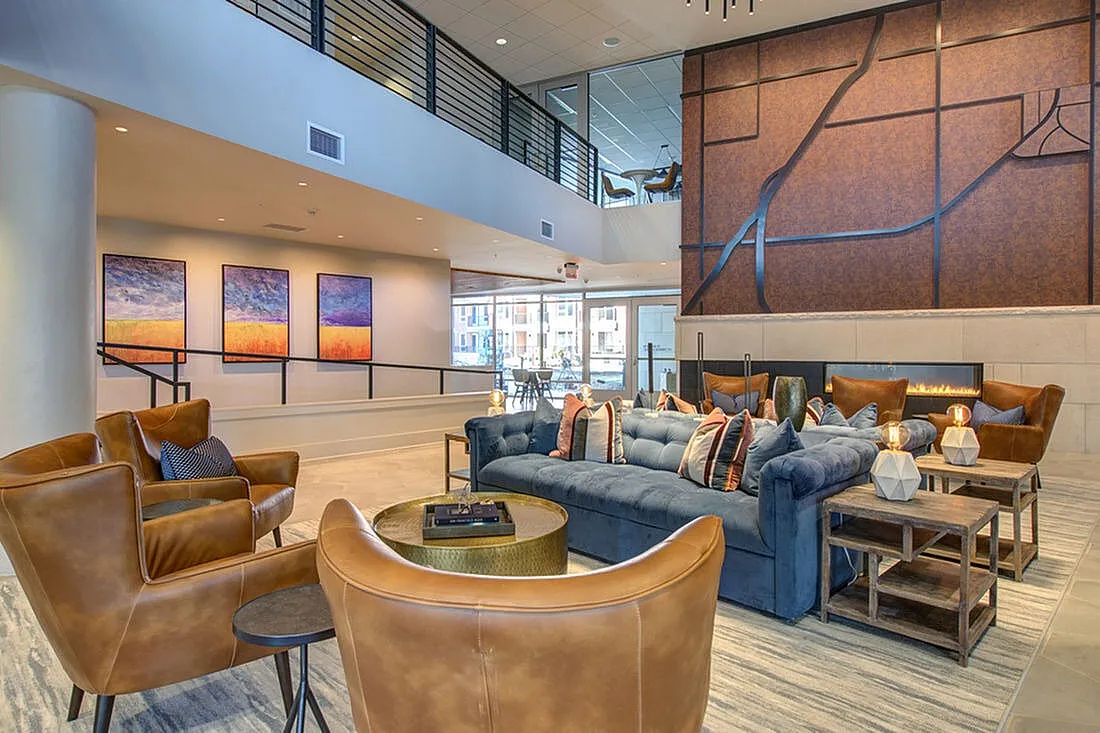 Luxurious apartment lobby featuring modern leather chairs, a plush blue sofa, and contemporary artwork with a stylish fireplace backdrop.