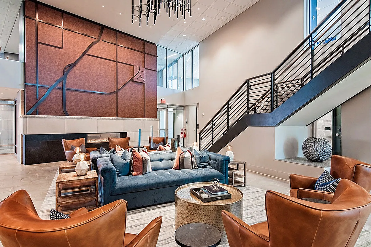 Modern and inviting apartment lobby showcasing a cozy seating area with plush blue sofa and stylish leather chairs, featuring elegant lighting and contemporary wall art.