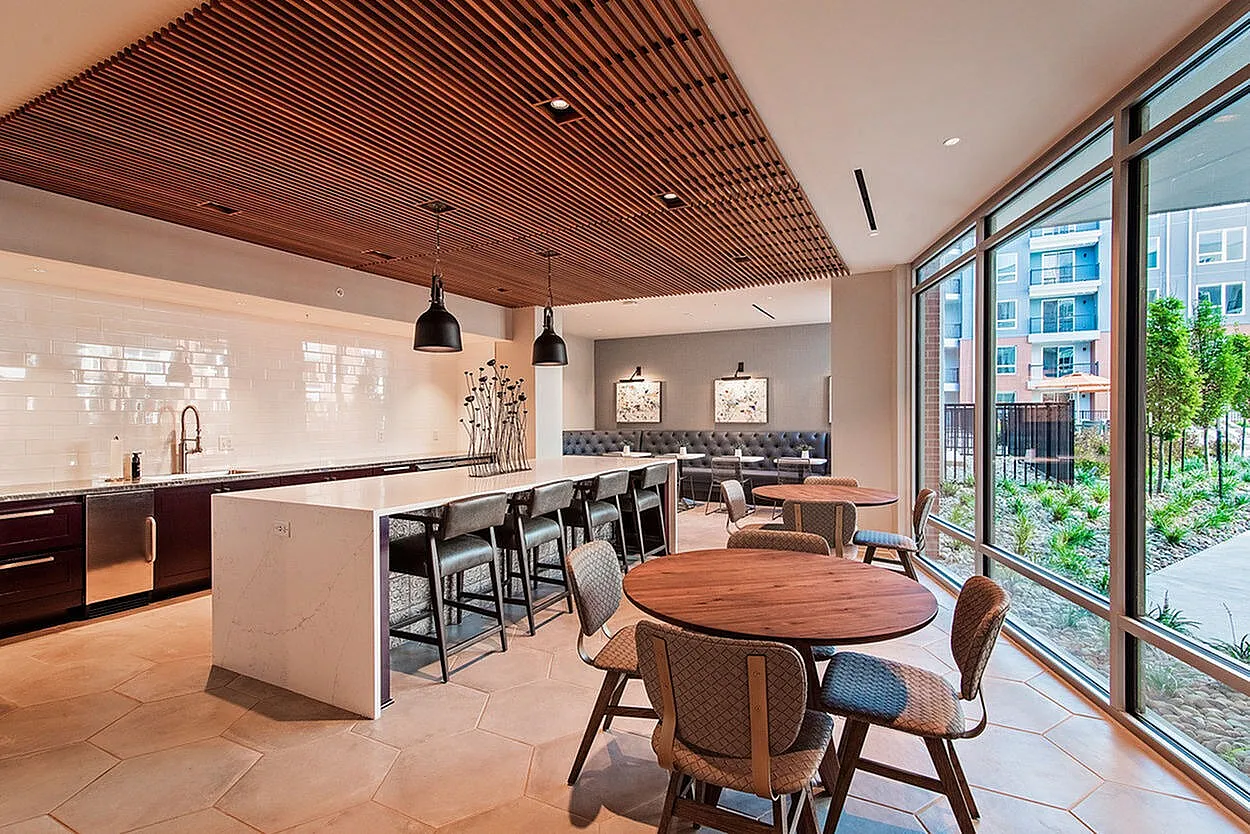 Modern communal area with sleek kitchen, elegant seating, and large windows offering garden views for a serene living experience.