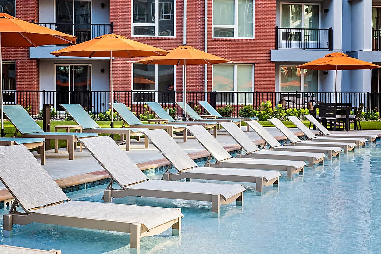 Elegant poolside lounge area with modern chaise lounges and vibrant orange umbrellas, perfect for relaxation and leisure.