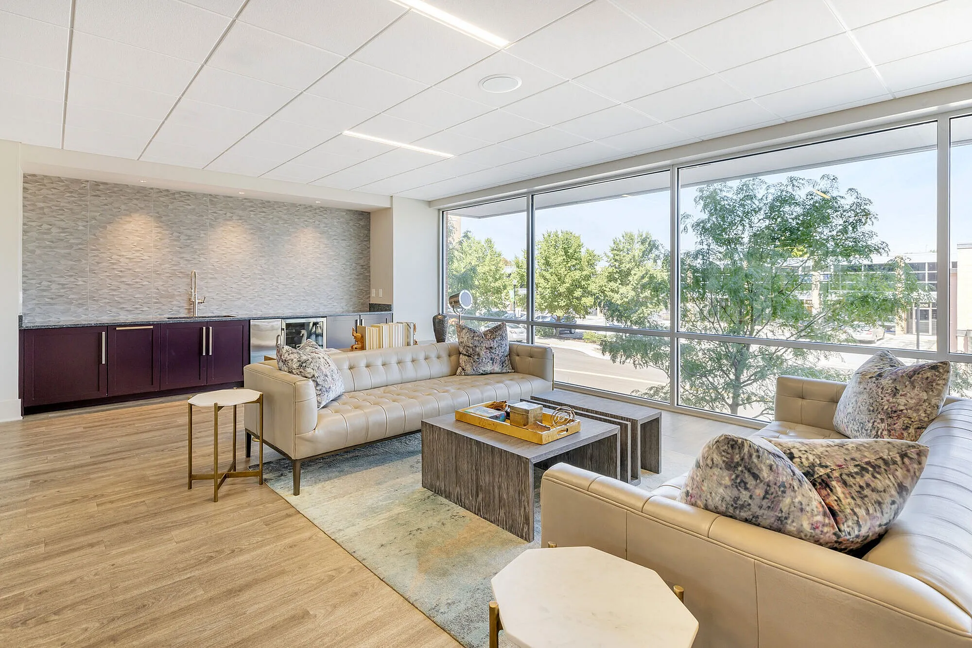 Sunlit living room with elegant leather sofas, floor-to-ceiling windows, and chic modern decor, offering a serene view of lush greenery.