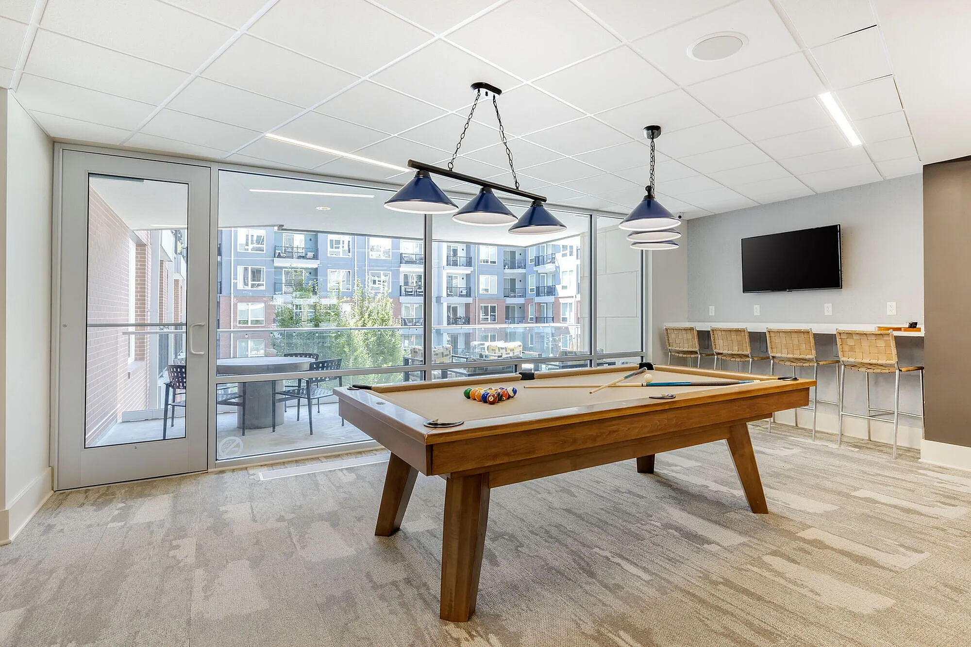 Chic recreational space featuring a pool table, modern lighting, a flat-screen TV, and large glass doors opening to a balcony with a view.