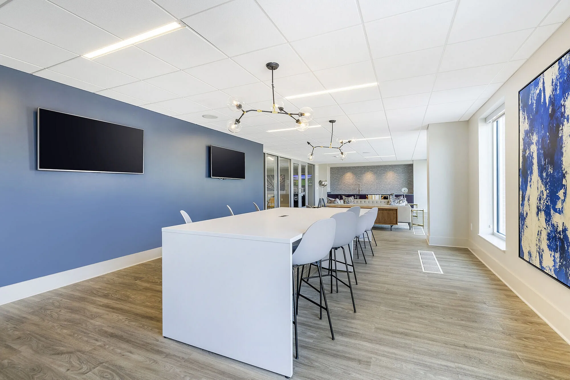Modern dining area with sleek white table, contemporary lighting, and vibrant blue accent wall in a stylish apartment.