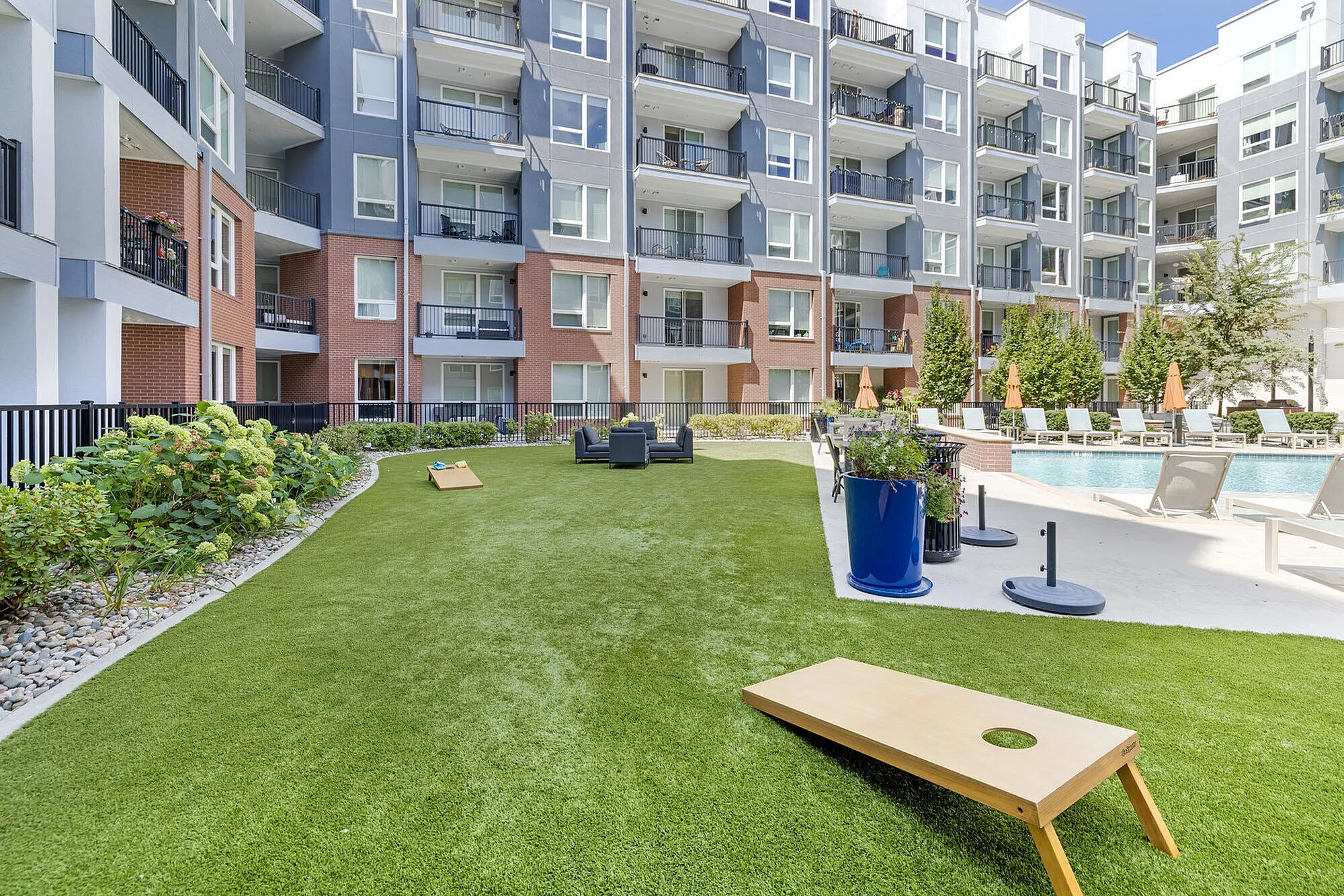 Modern apartment complex with vibrant outdoor area, featuring a lush green lawn, stylish lounge chairs, and a sparkling swimming pool perfect for relaxation.