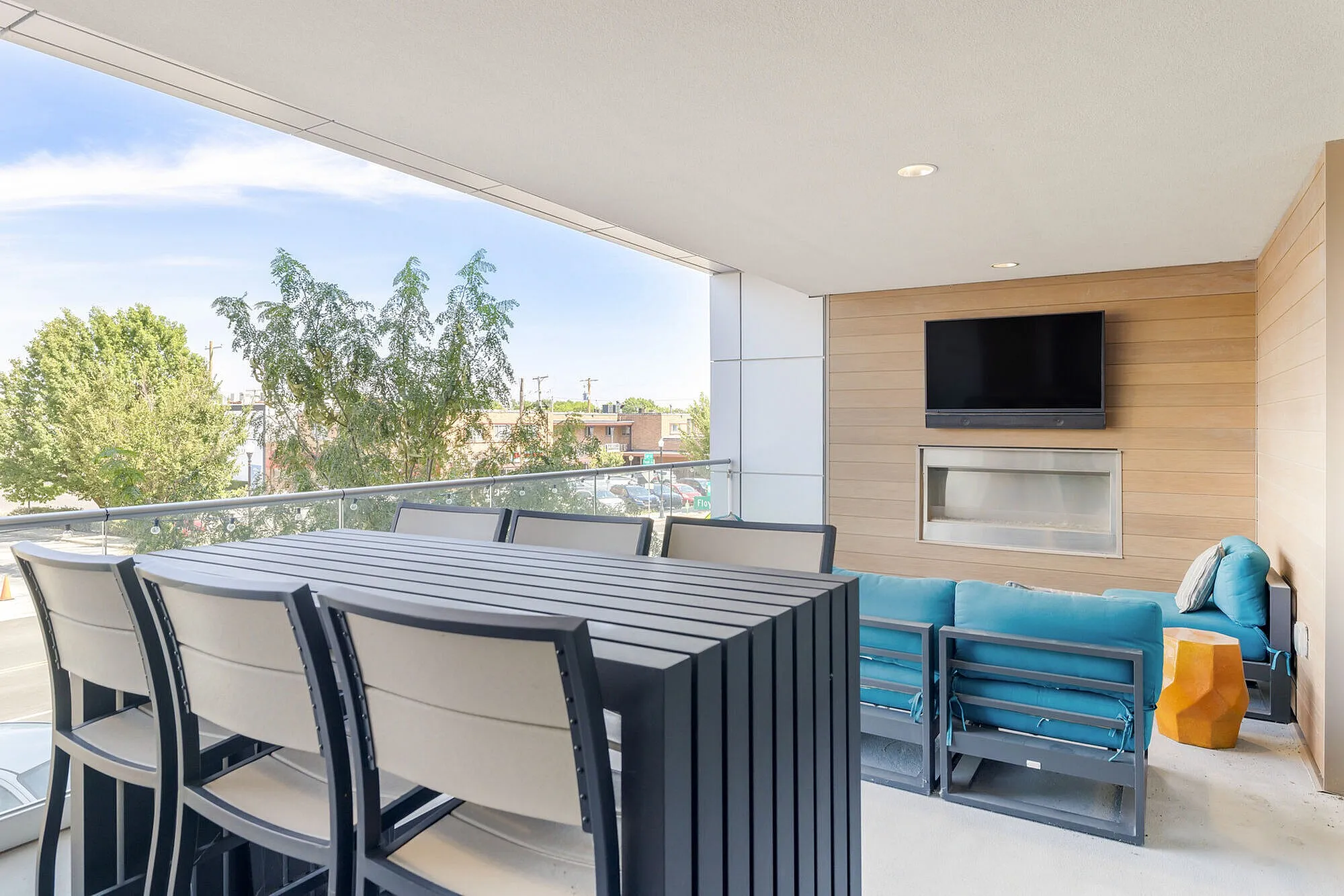 Contemporary outdoor balcony with comfortable seating, wooden accent wall, and mounted TV, offering a scenic view for relaxation or entertainment.
