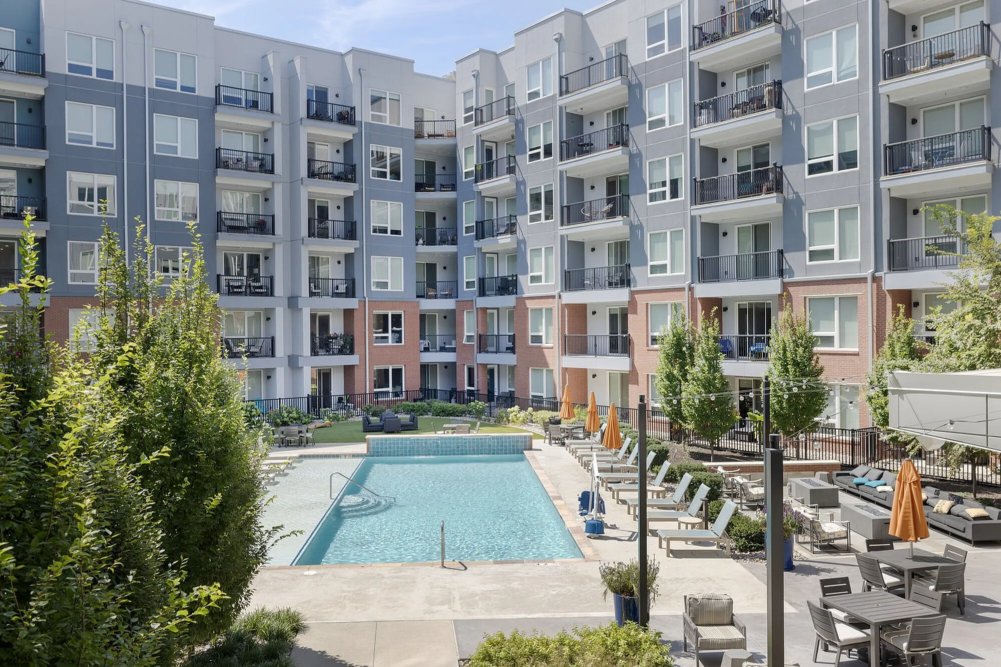Modern apartment complex with a luxurious outdoor swimming pool, surrounded by lush greenery and stylish lounge areas, perfect for relaxation and social gatherings.