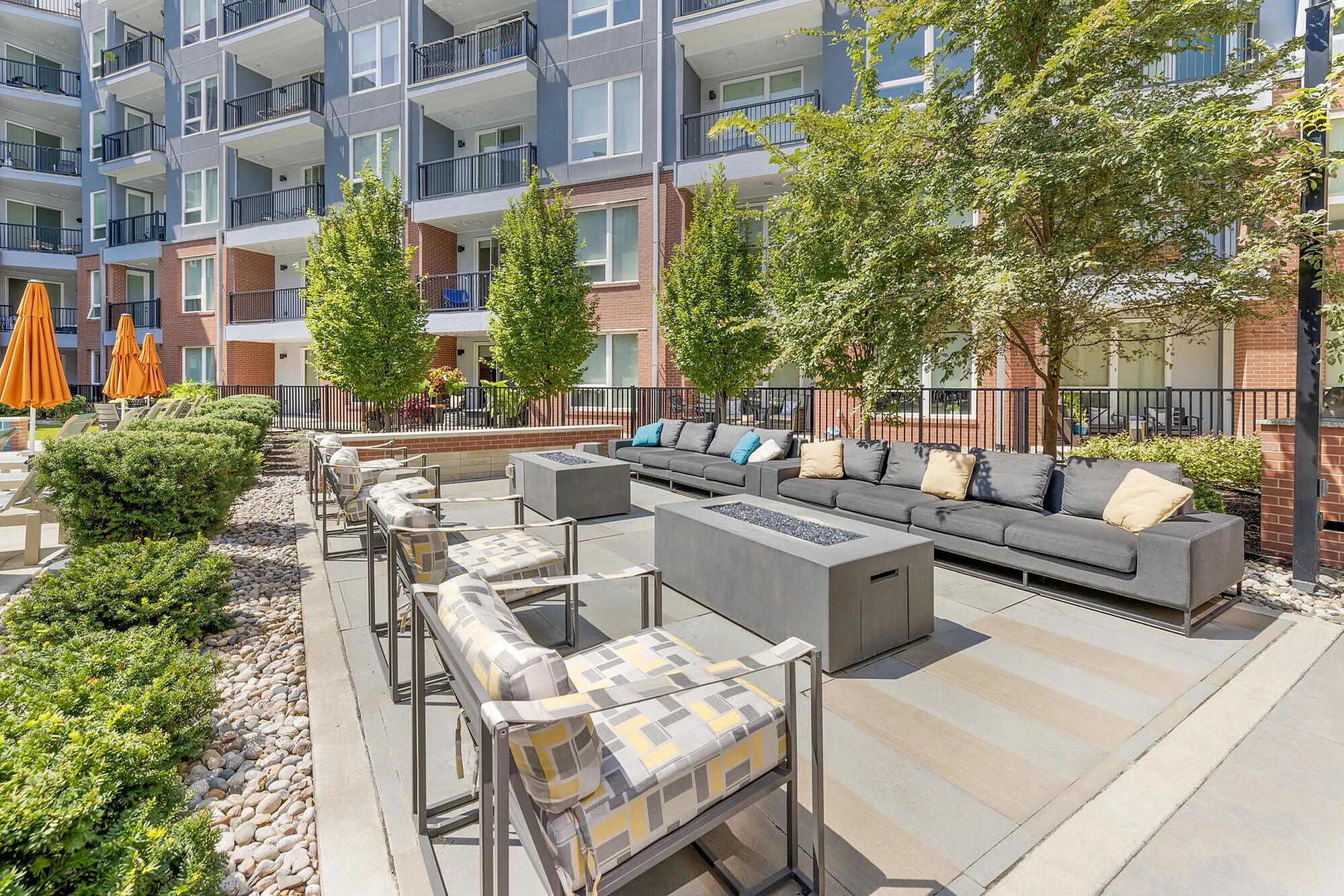 Chic outdoor living space with modern seating, lush greenery, and vibrant orange umbrellas, perfect for relaxation and social gatherings.