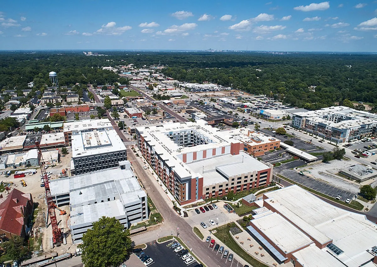 Aerial view of a vibrant cityscape with modern apartment complexes, surrounded by lush greenery and clear blue skies.