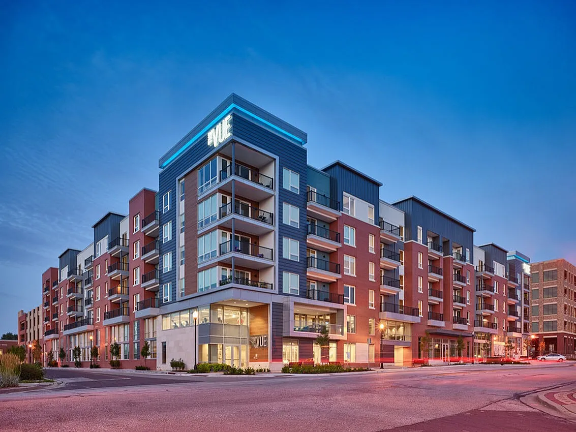 Modern apartment building with stylish balconies and vibrant brick facade at sunset, offering urban living at its finest.