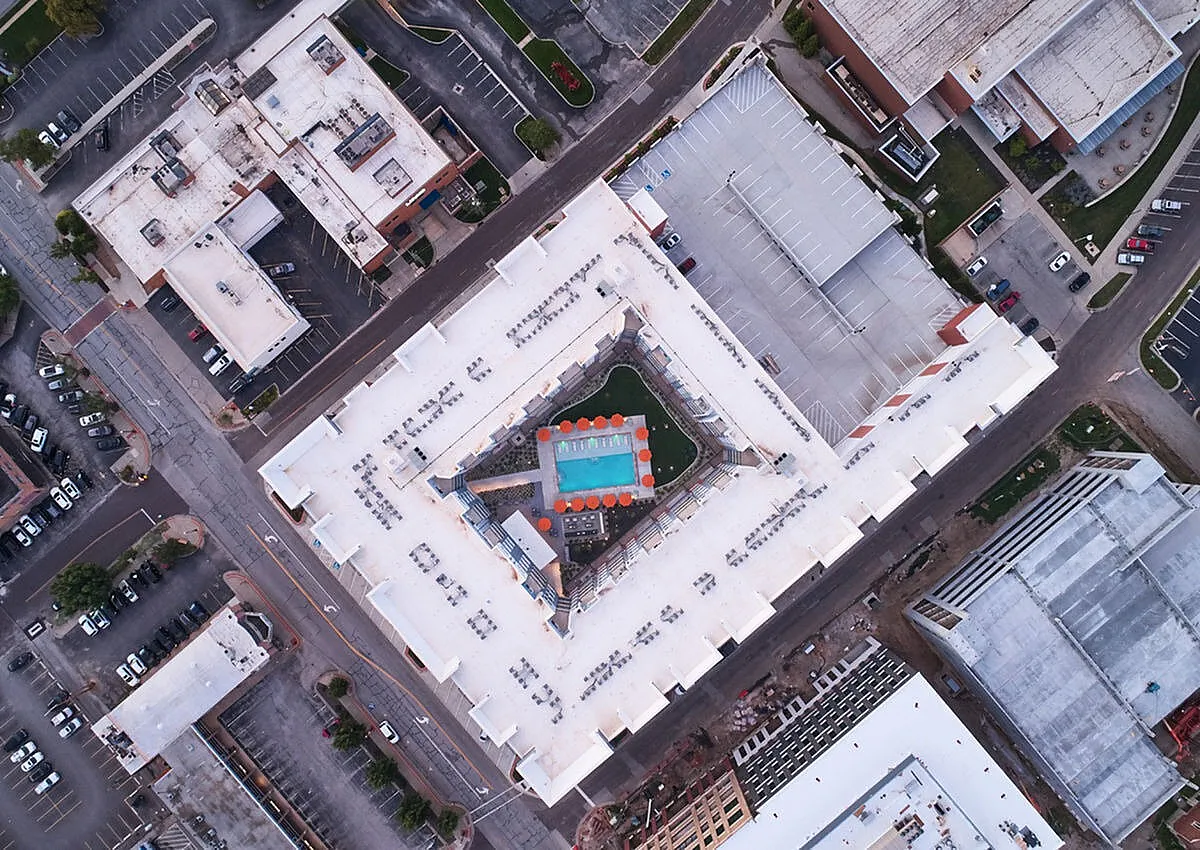 Aerial view of a modern apartment complex featuring a lush central courtyard with a sparkling pool, surrounded by vibrant cityscape.