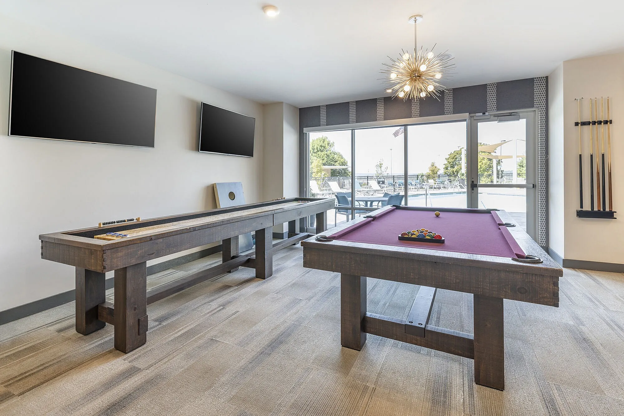 Chic game room with a purple pool table, shuffleboard, modern lighting, and poolside view through large windows.