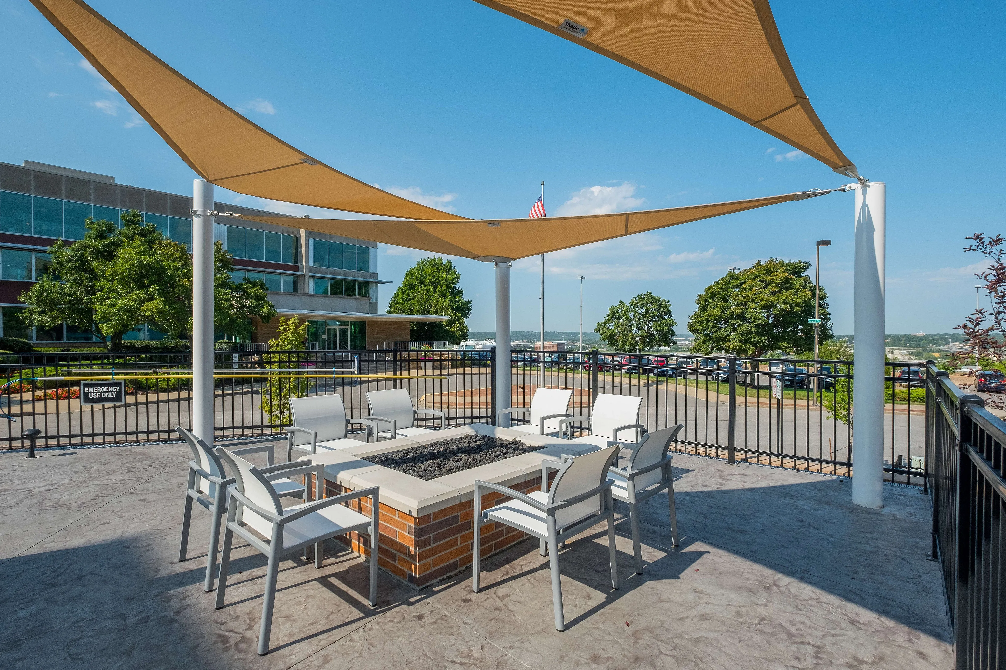 Modern outdoor lounge with stylish chairs surrounding a central fire pit, shaded by elegant triangular sails, offering a relaxing and inviting atmosphere.