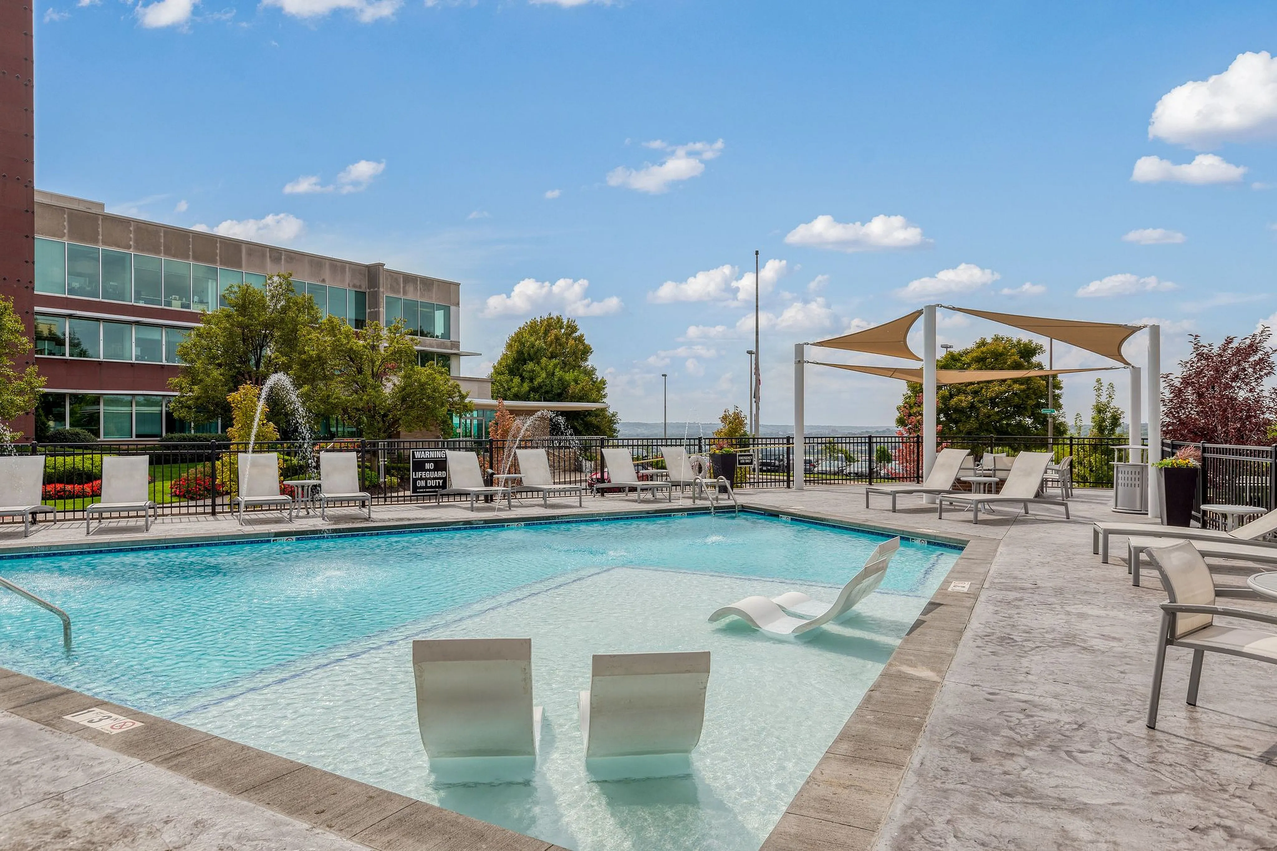 Chic outdoor pool area featuring elegant lounge chairs, water fountains, and modern architectural design with vibrant landscaping.