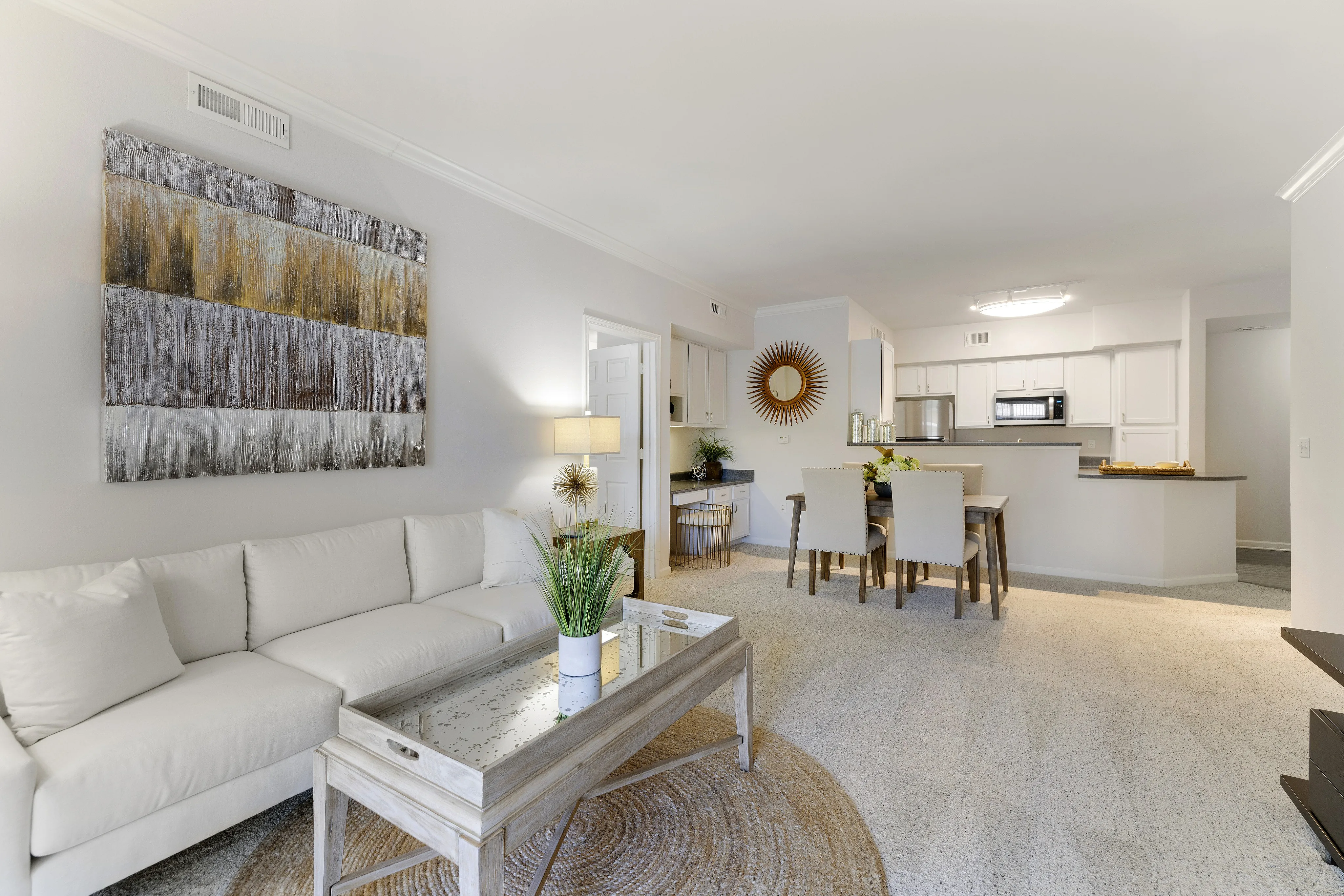 Elegant open-concept living space with a plush white sofa, modern artwork, and a chic dining area leading to a stylish kitchen.