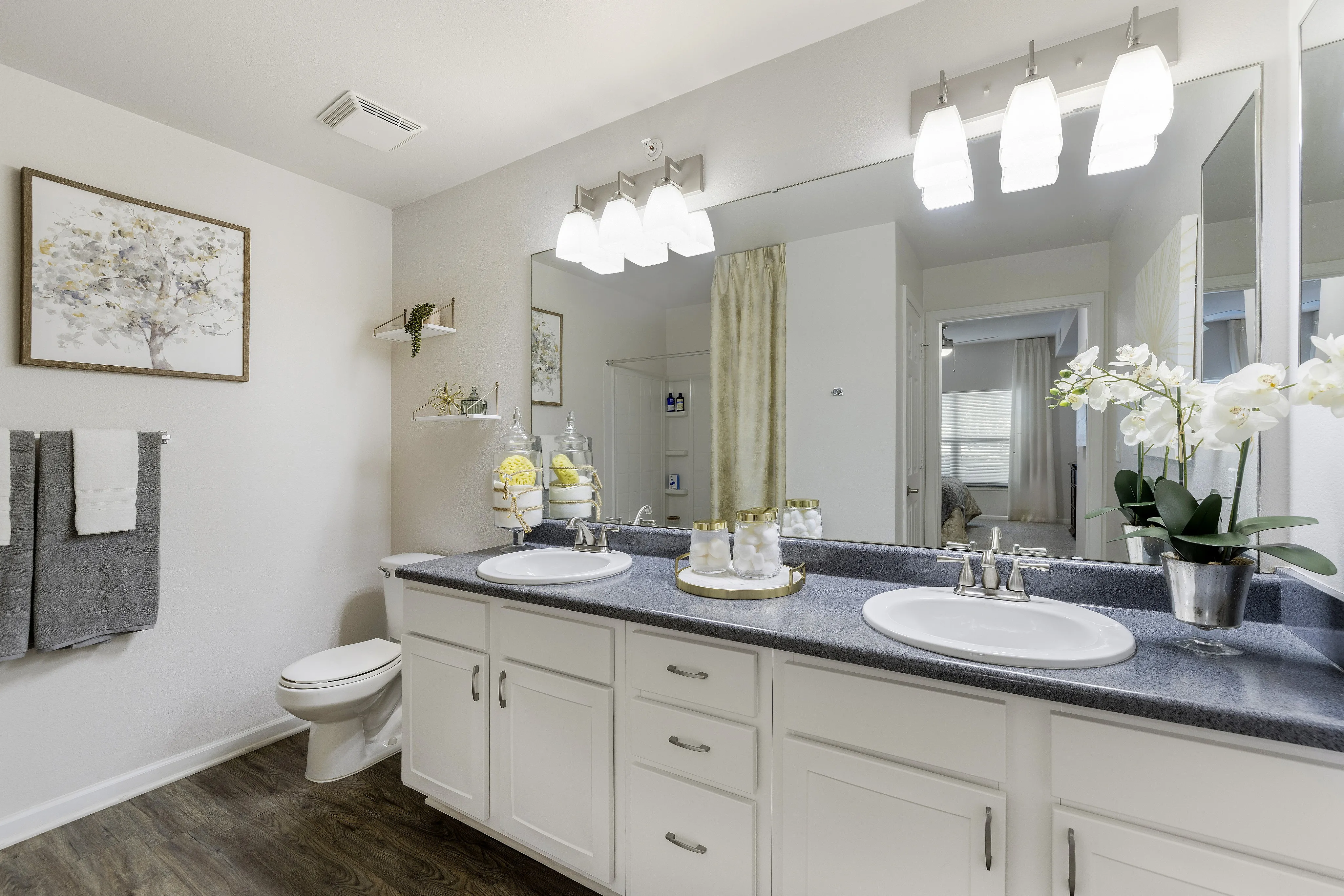 Elegant bathroom with dual sinks, modern lighting, and stylish decor, featuring white cabinetry and sleek countertops.