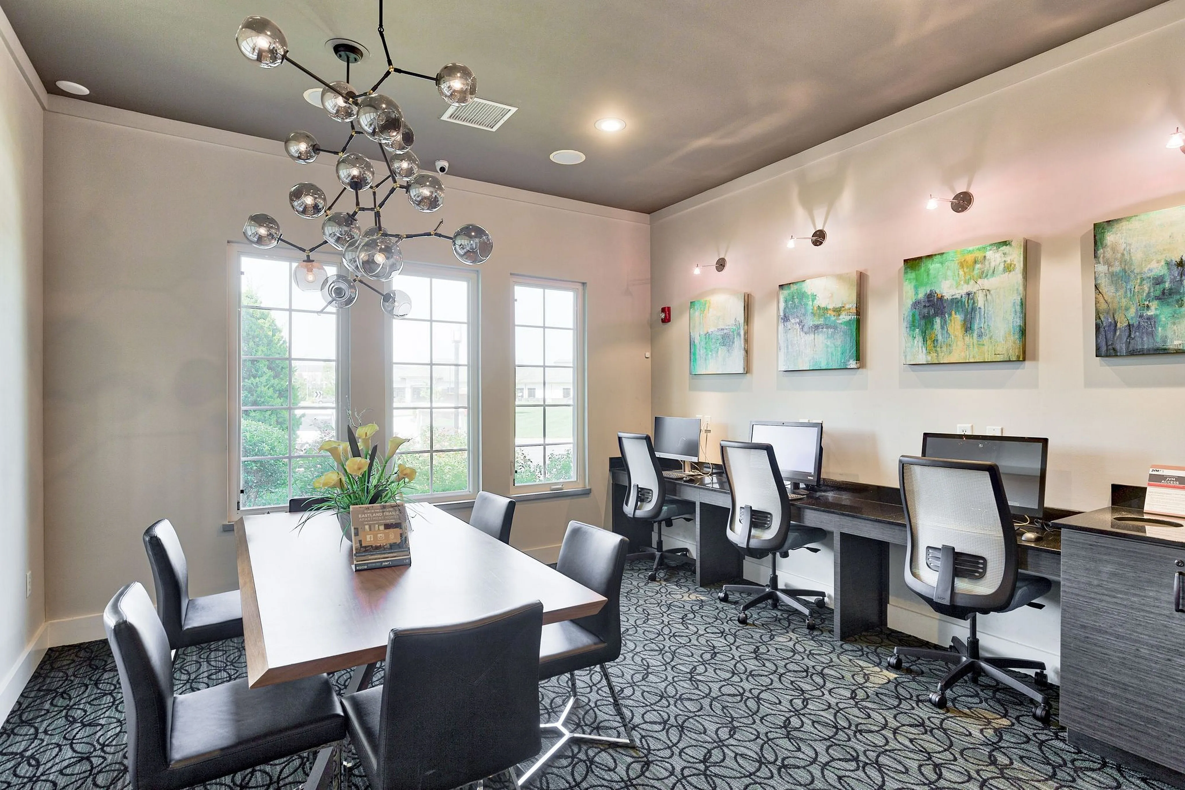 Sophisticated co-working space featuring modern office chairs, sleek desks, artistic lighting, and vibrant abstract artwork, set against large windows for natural light.