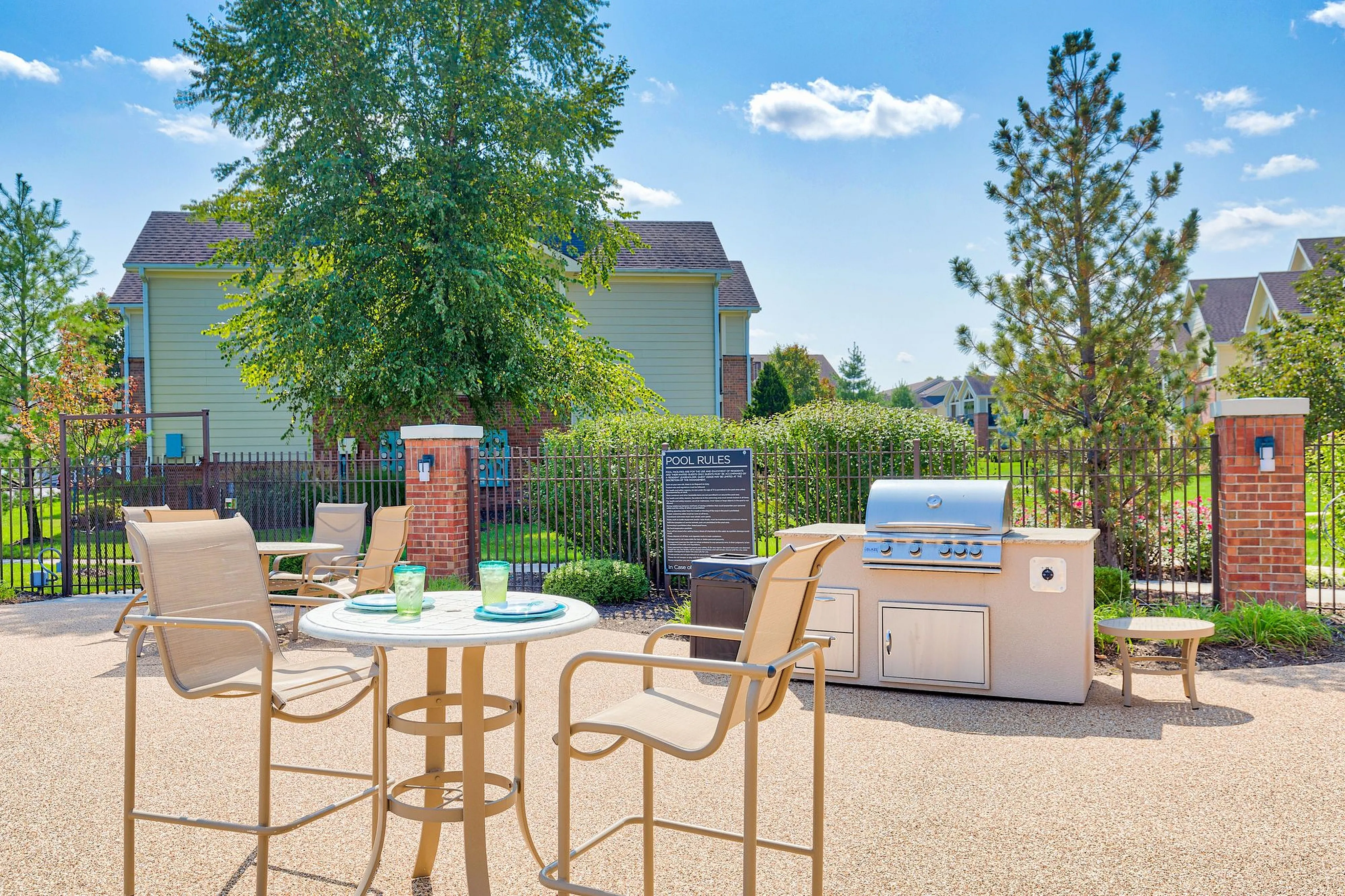 Vibrant outdoor patio featuring comfortable seating, a modern grill, and lush landscaping under a clear blue sky.