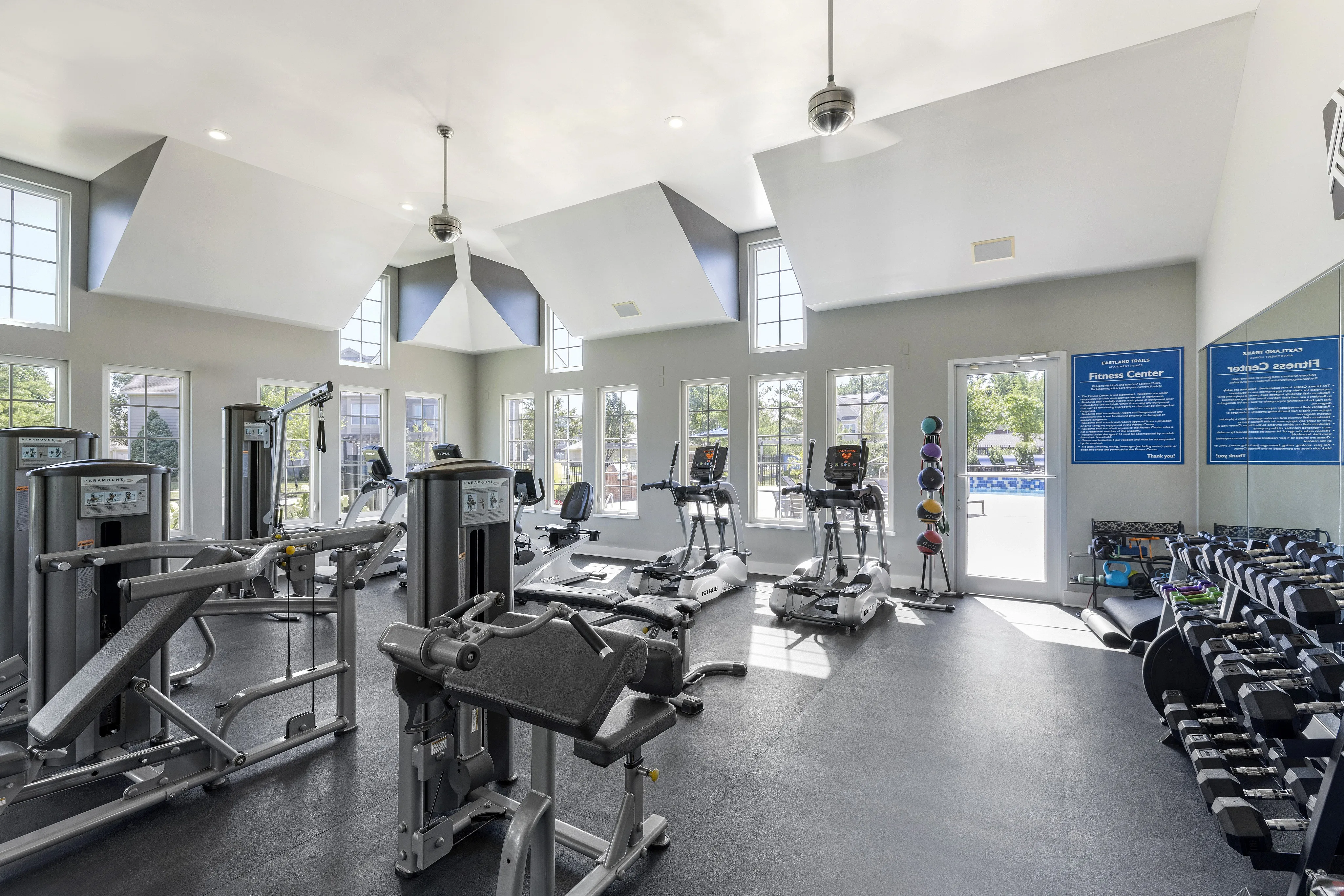 Bright and modern fitness center with high ceilings, state-of-the-art exercise machines, and ample natural light through large windows.