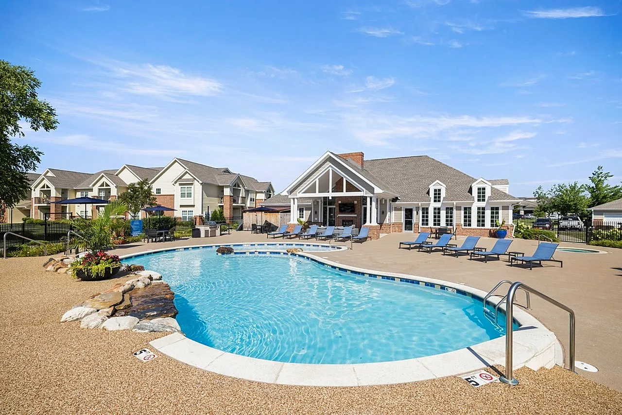 Inviting community pool area with lush landscaping, modern poolside seating, and a charming clubhouse under a clear blue sky.