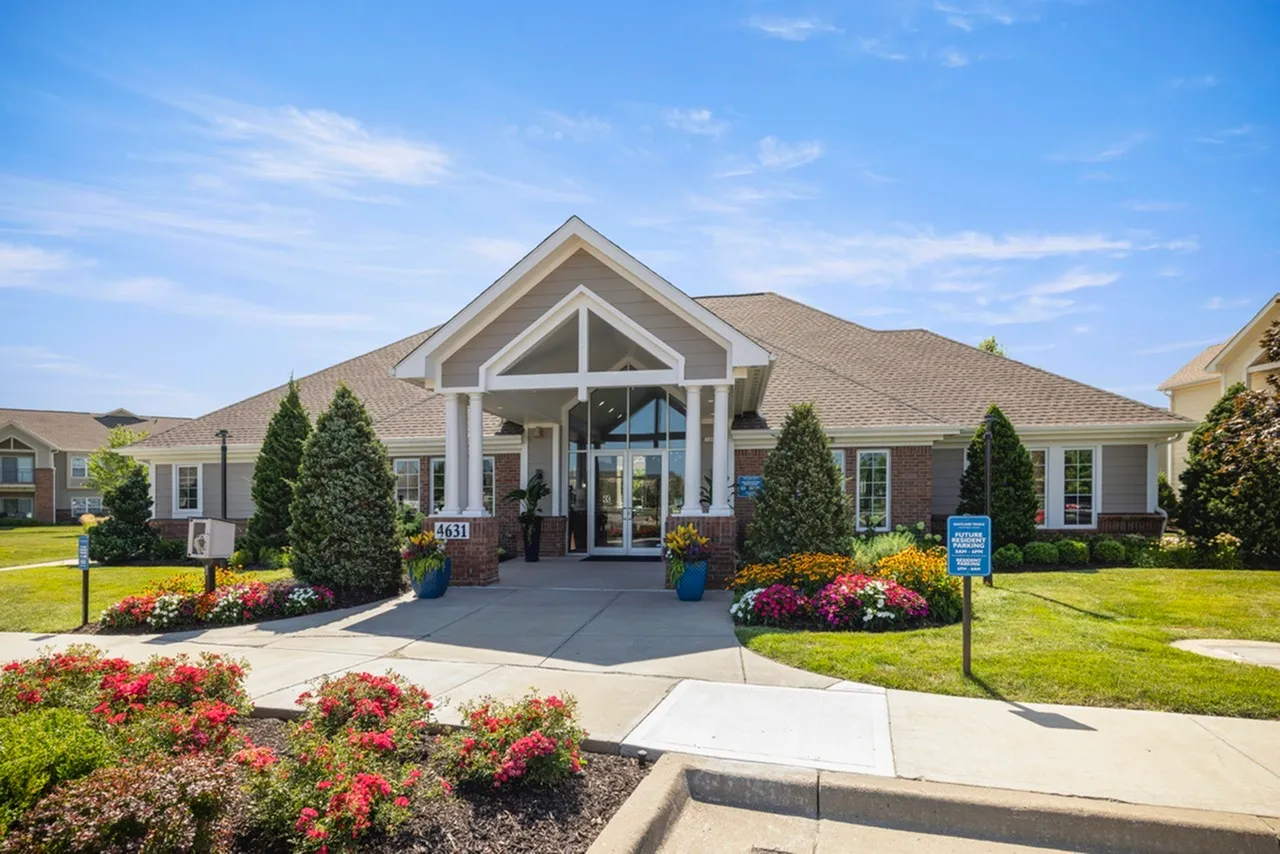 Charming residential building with elegant entrance, lush landscaping, and vibrant flower gardens under a clear blue sky.