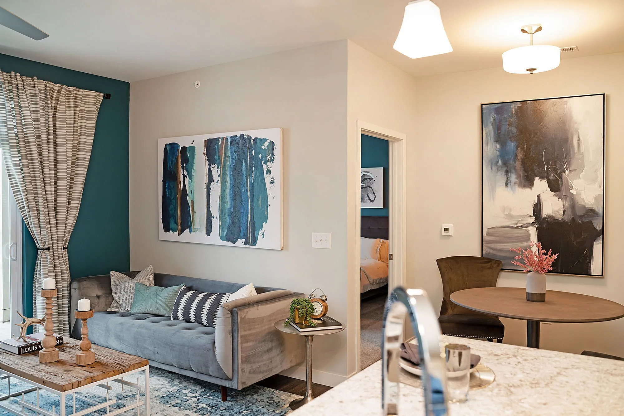 Chic and modern apartment living room with elegant decor, featuring a cozy gray sofa, stylish artwork, and a warm dining nook.