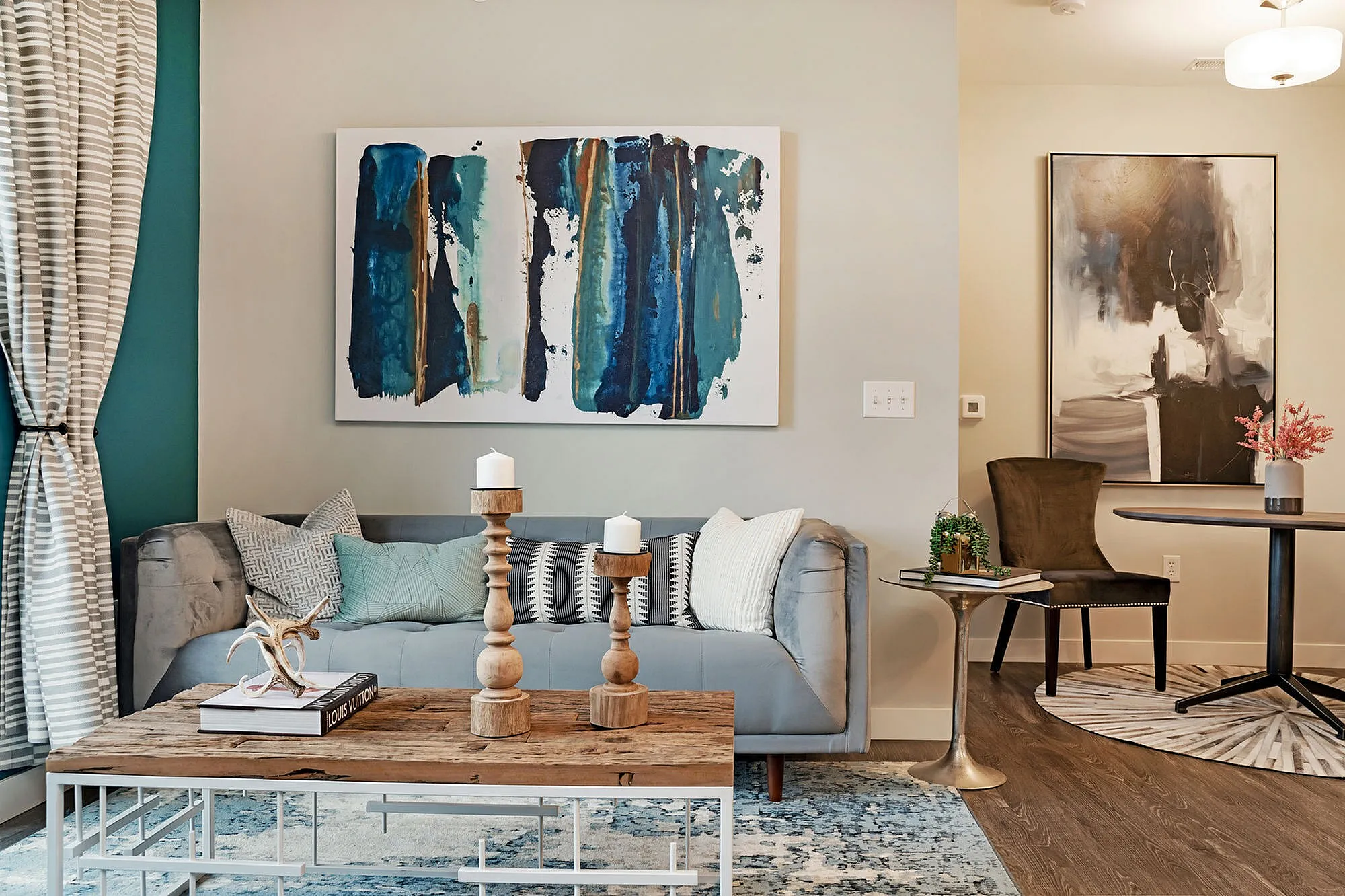 Chic living room with a stylish gray sofa, vibrant blue abstract art, and a rustic wooden coffee table, offering a cozy, modern ambiance.