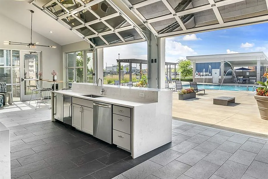 Modern open kitchen with sleek appliances leading to a sunlit patio and swimming pool view.